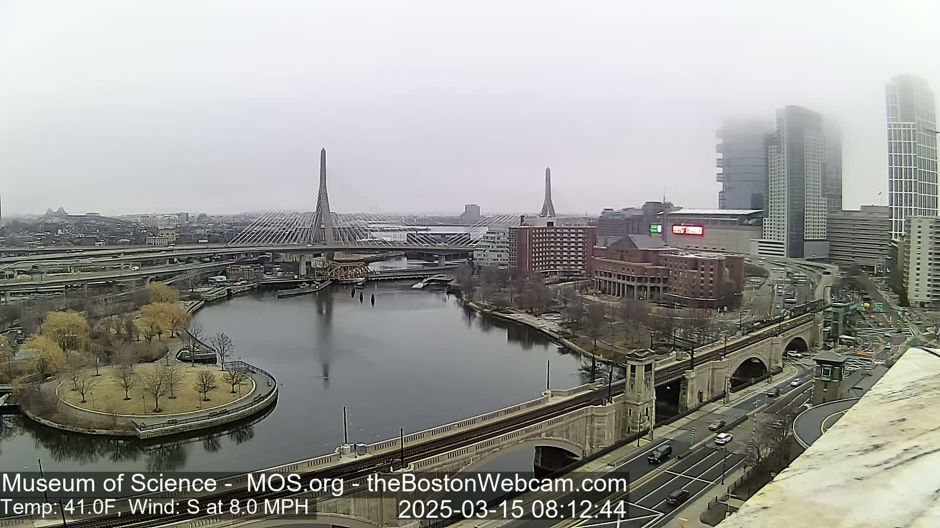 A foggy cityscape shows a river, two cable-stayed bridges, and several buildings, with a temperature of 41 degrees Fahrenheit and a south wind of 8 miles per hour.