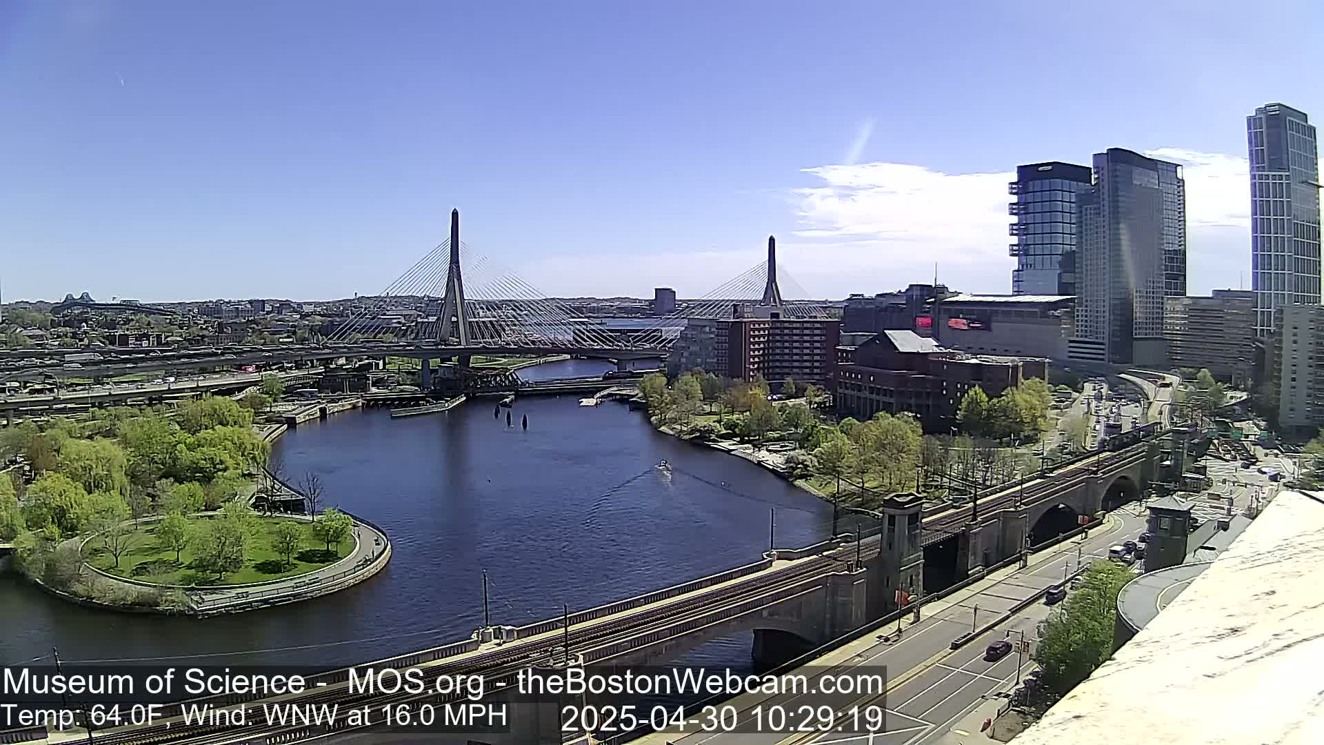 A sunny day reveals a cityscape with two cable-stayed bridges spanning a river, surrounded by green spaces, buildings, and roadways.