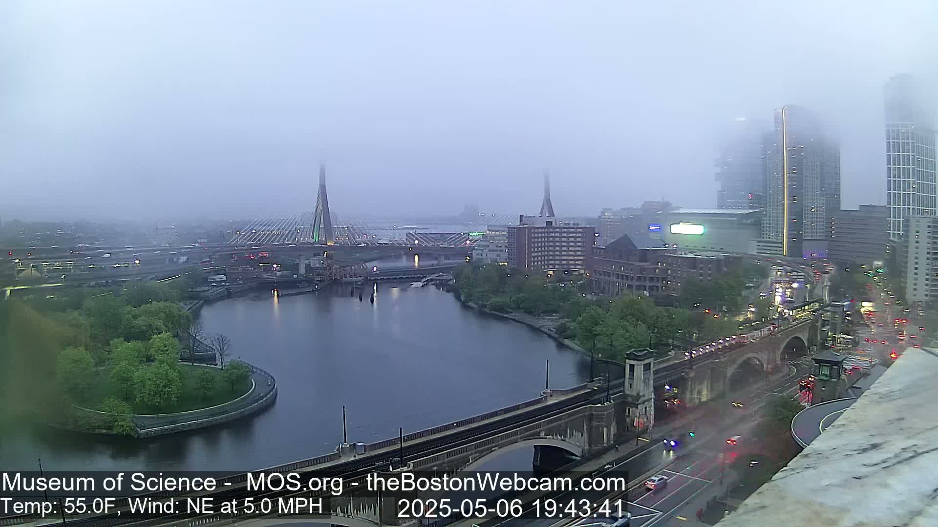 A foggy cityscape with bridges spanning a river, featuring buildings and roadways under a hazy sky.