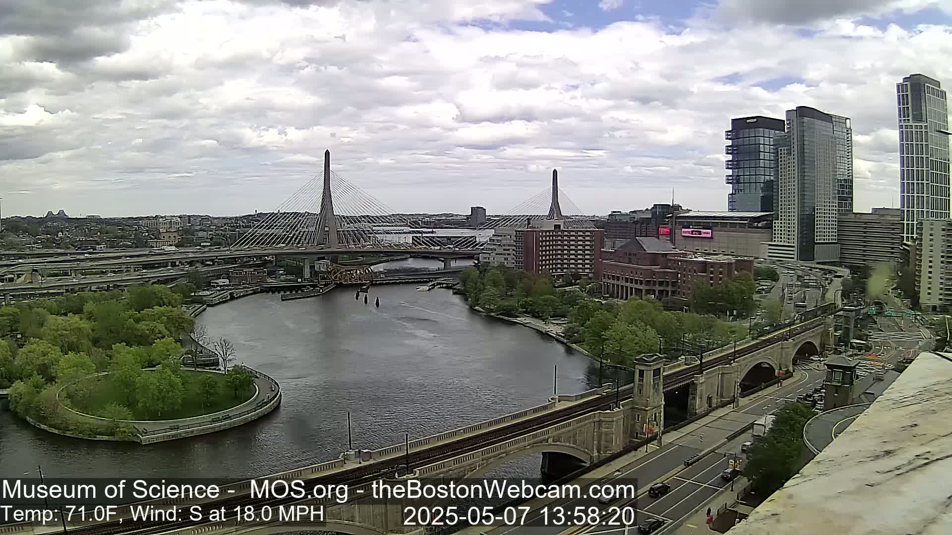 A cloudy day shows a cityscape with two cable-stayed bridges spanning a river, along with a train bridge and various buildings, including high-rises.