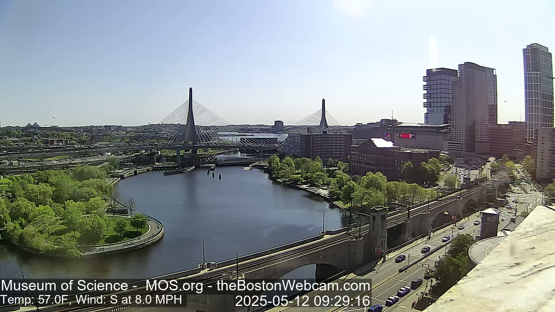 A sunny day reveals a cityscape with two cable-stayed bridges spanning a river, surrounded by green trees and modern buildings.