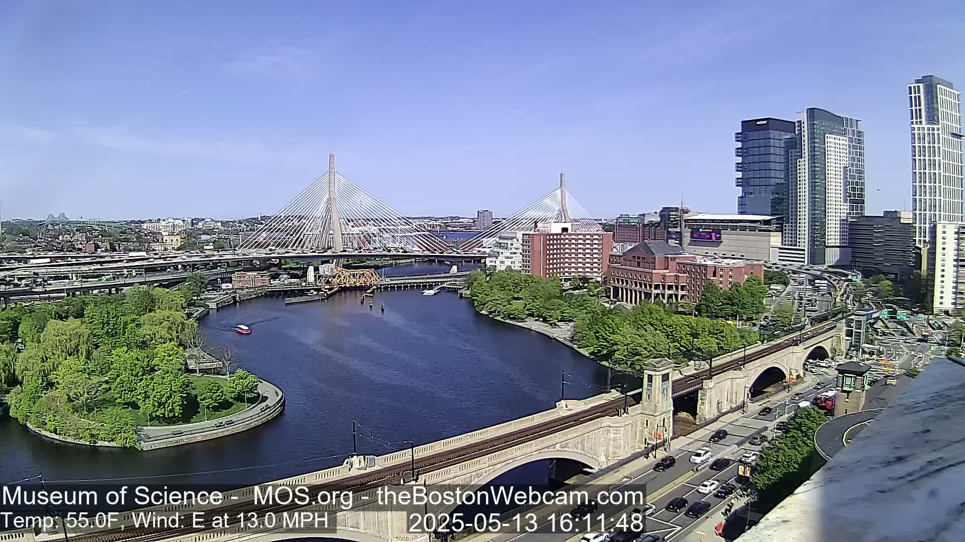 A sunny day reveals a city landscape with two cable-stayed bridges spanning a river, alongside a train bridge and numerous buildings, including tall skyscrapers.