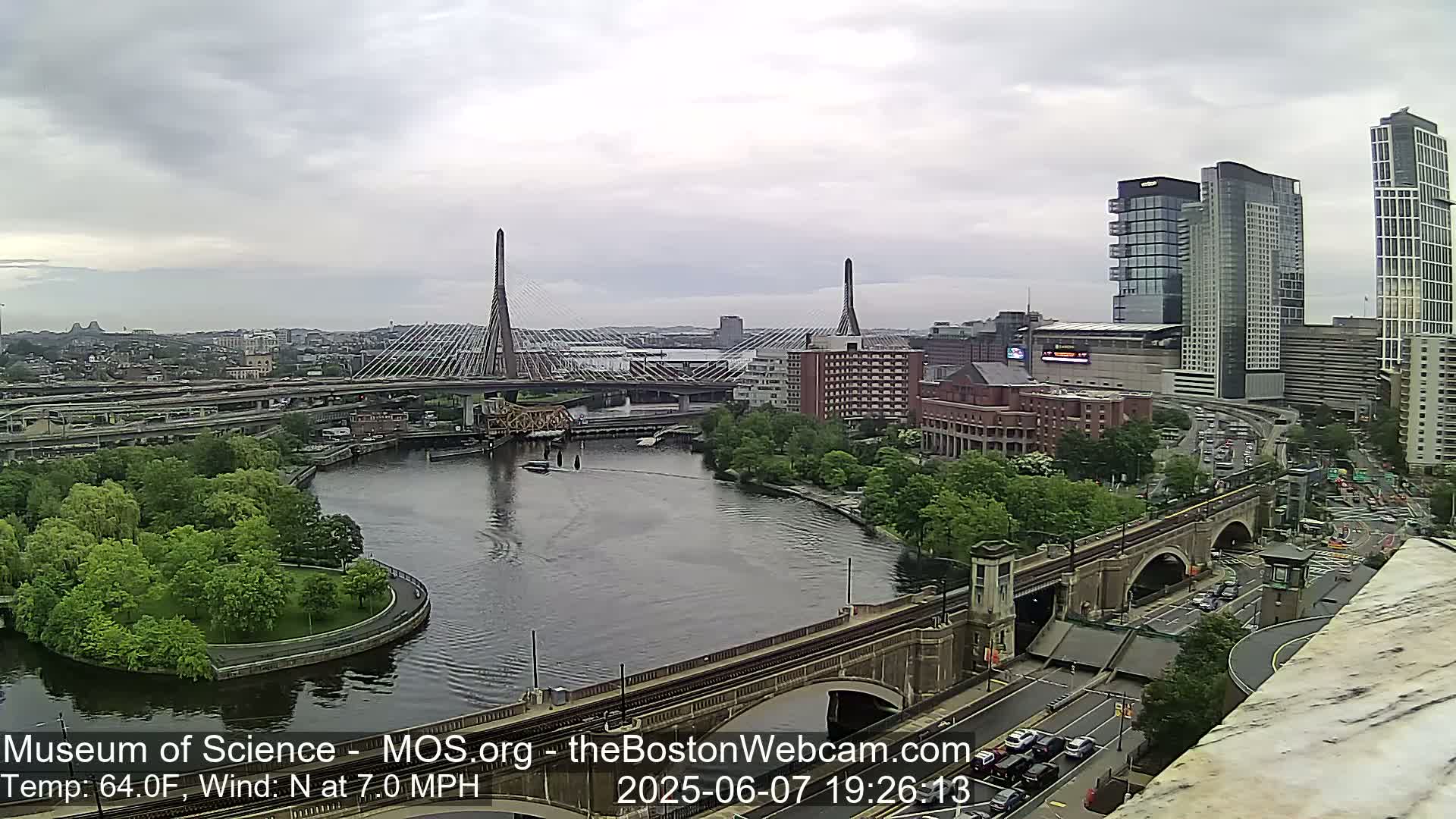 A cityscape with a river, bridges, and lush green trees under an overcast sky.