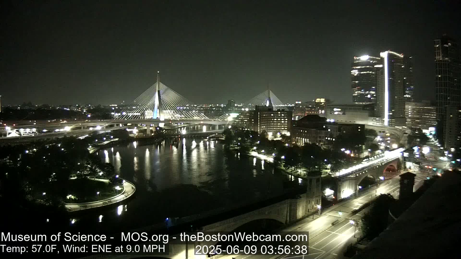 A nighttime view of a city with two cable-stayed bridges spanning a river, under a clear, dark sky.