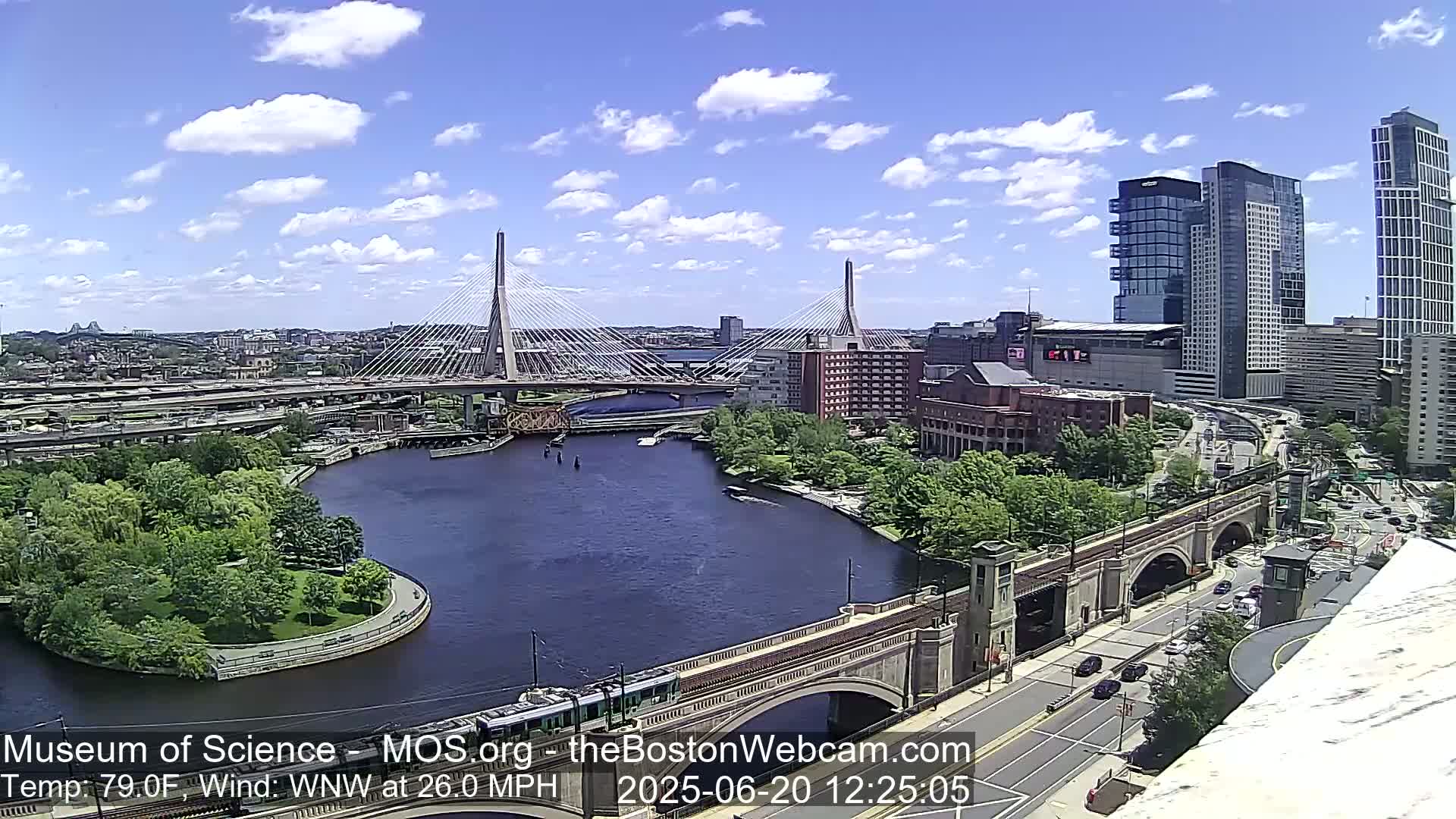 A sunny day reveals a cityscape with two cable-stayed bridges spanning a river, alongside a stone arch bridge and modern high-rises, all under a partly cloudy sky.