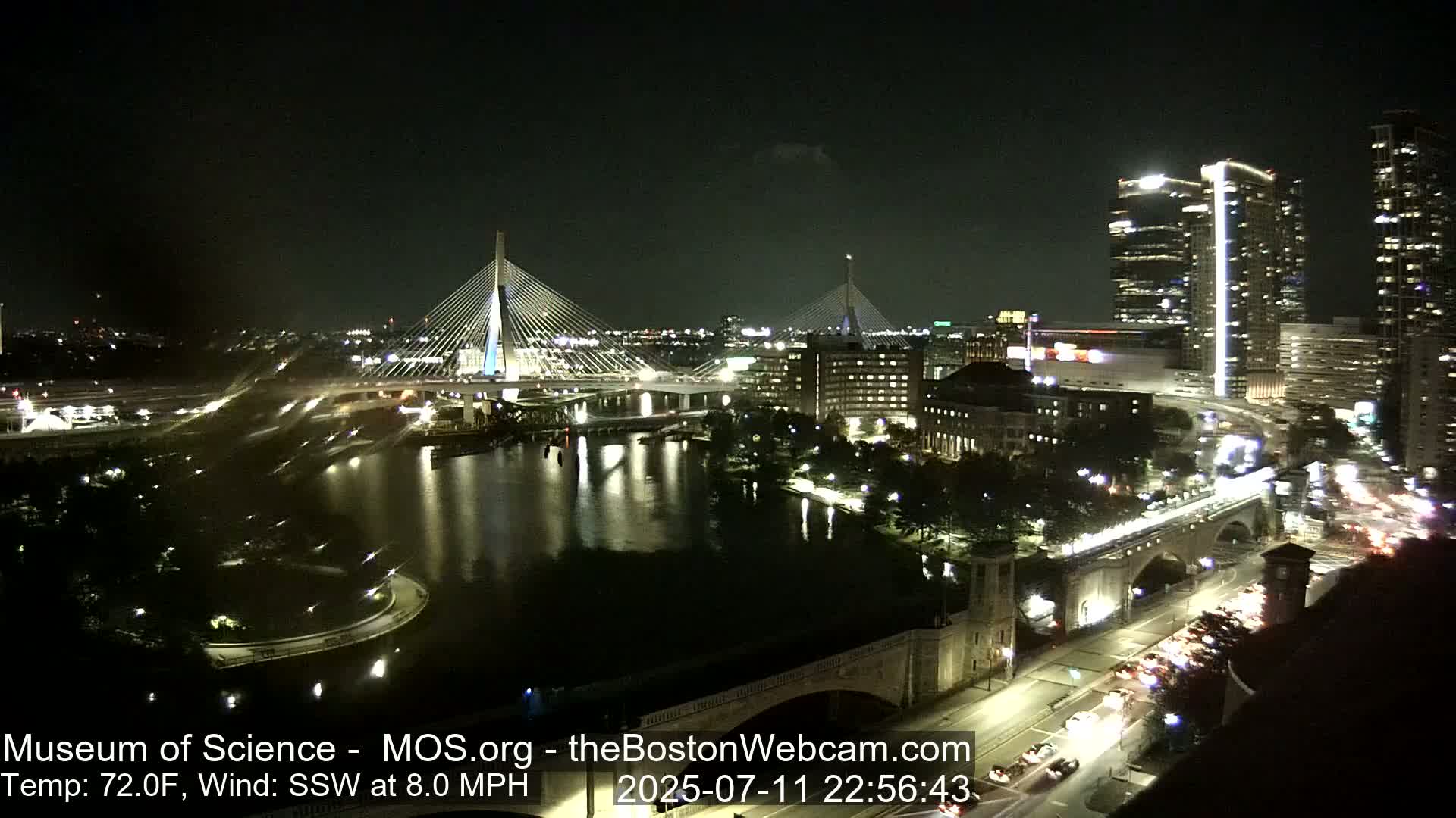 A nighttime cityscape with a bridge and river, shrouded in fog under a dark sky.