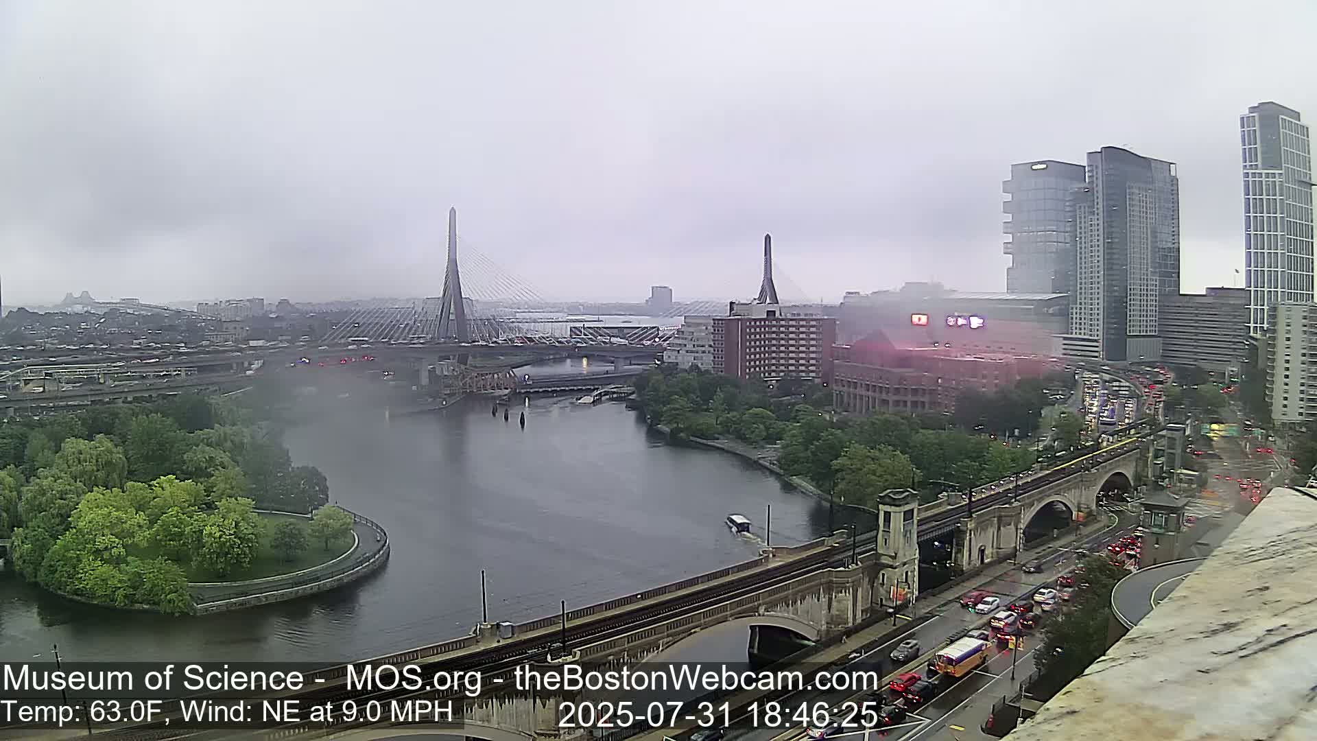 A rainy cityscape shows two bridges spanning a river, with traffic on the roads and a cityscape in the background.