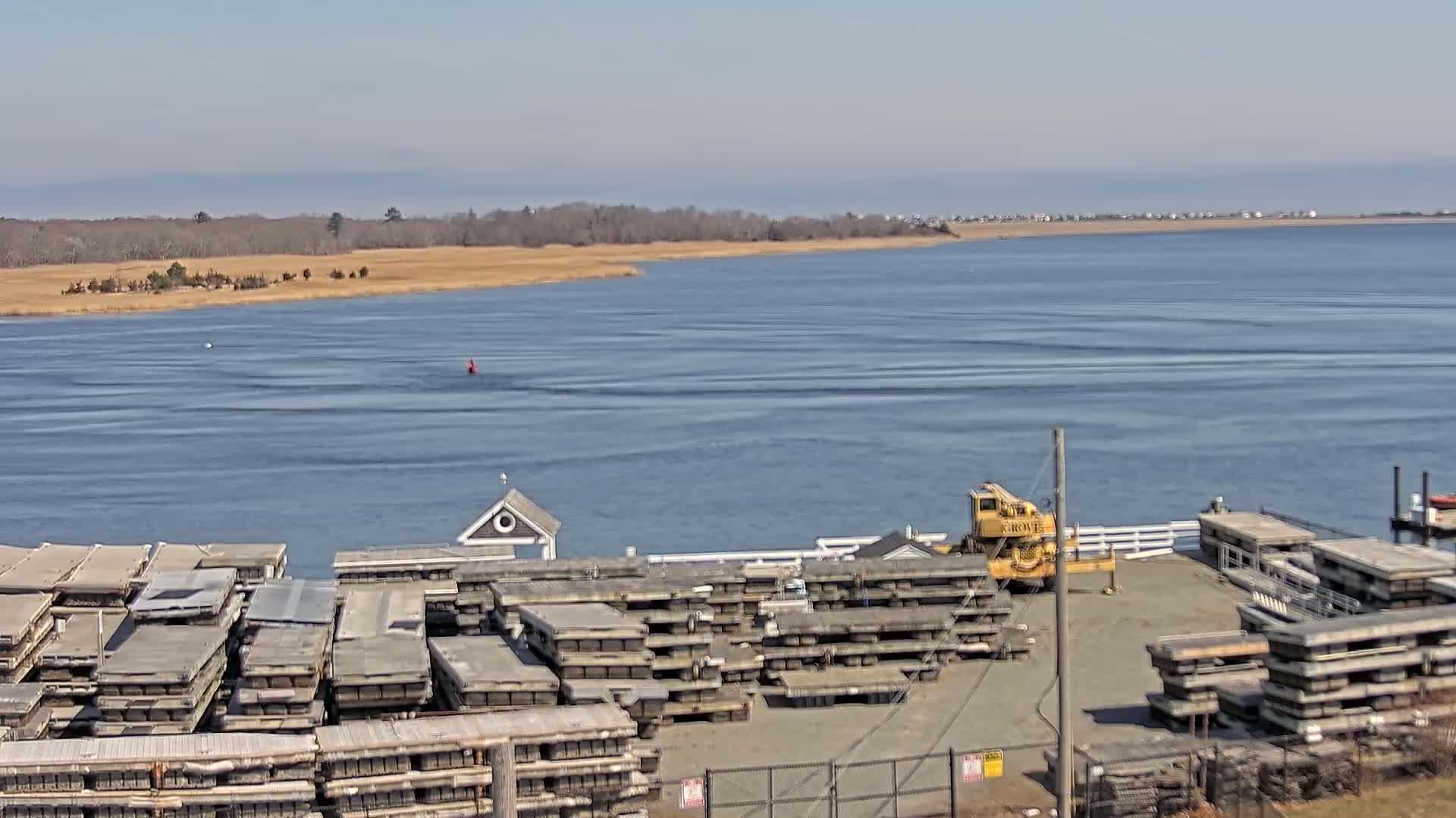 A calm body of water is seen with stacked floating docks and a small crane on the shore under a clear sky.