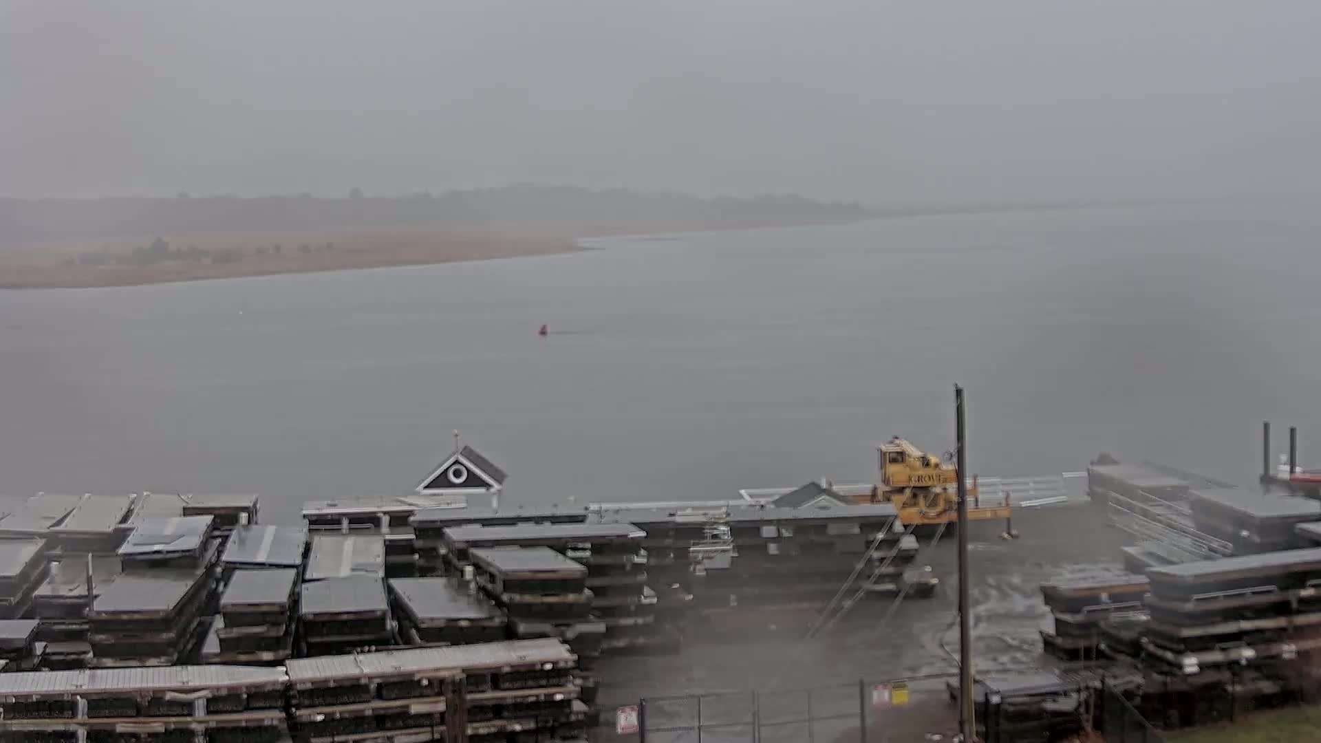 A hazy, overcast day reveals a body of water with stacked barges and a crane at a dock.