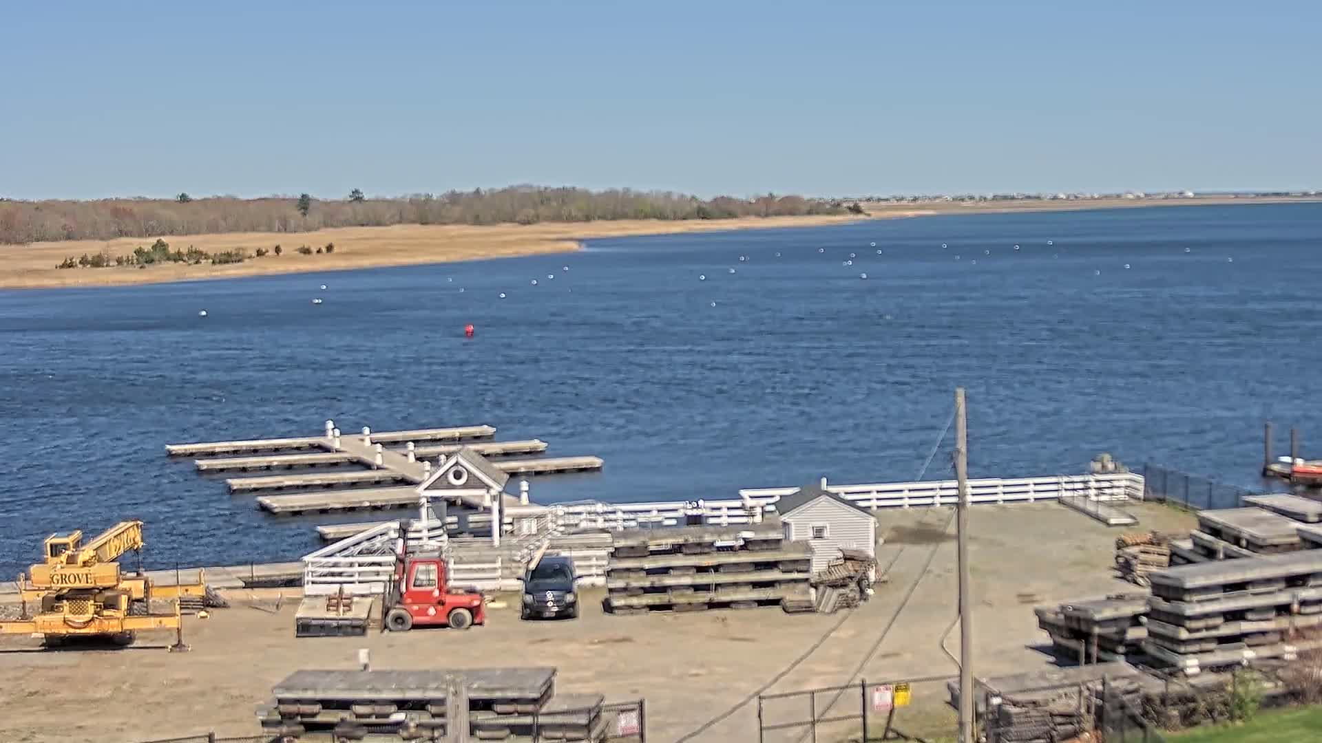 A body of water with a dock and several pieces of construction equipment is seen on a sunny day.