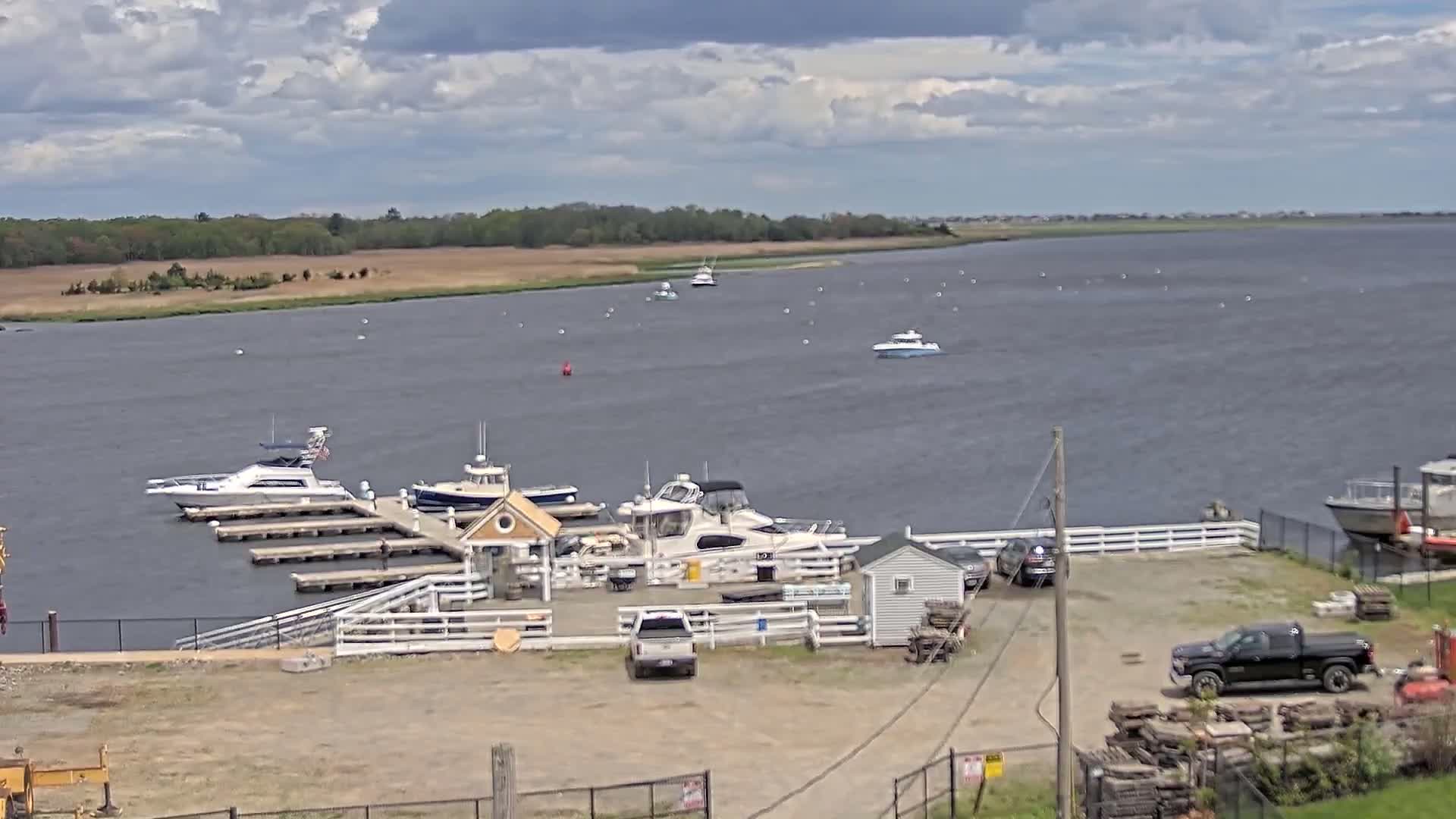 A marina with several boats docked at a waterfront location under a partly cloudy sky.