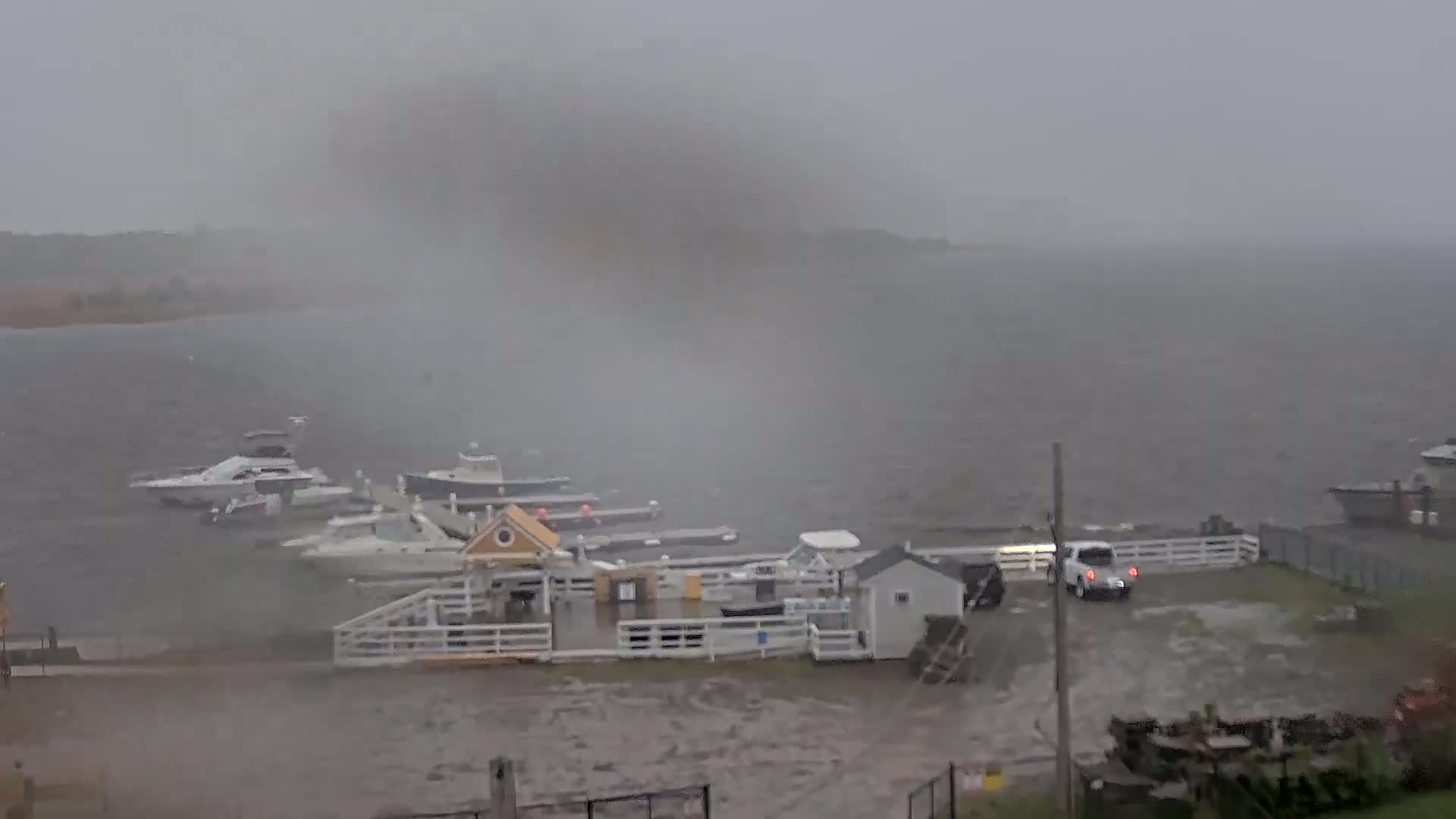 A small marina with several boats is partially submerged in floodwaters during a heavy storm.
