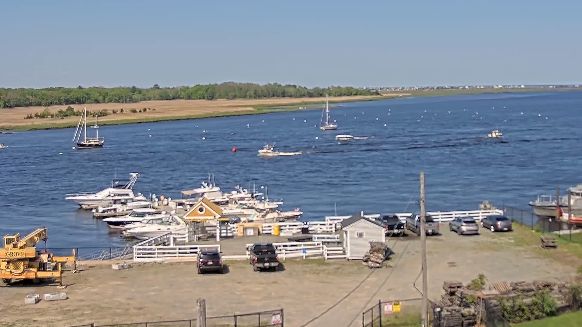 A marina with several motorboats and sailboats docked, under a clear blue sky, on a calm body of water with other boats further out.
