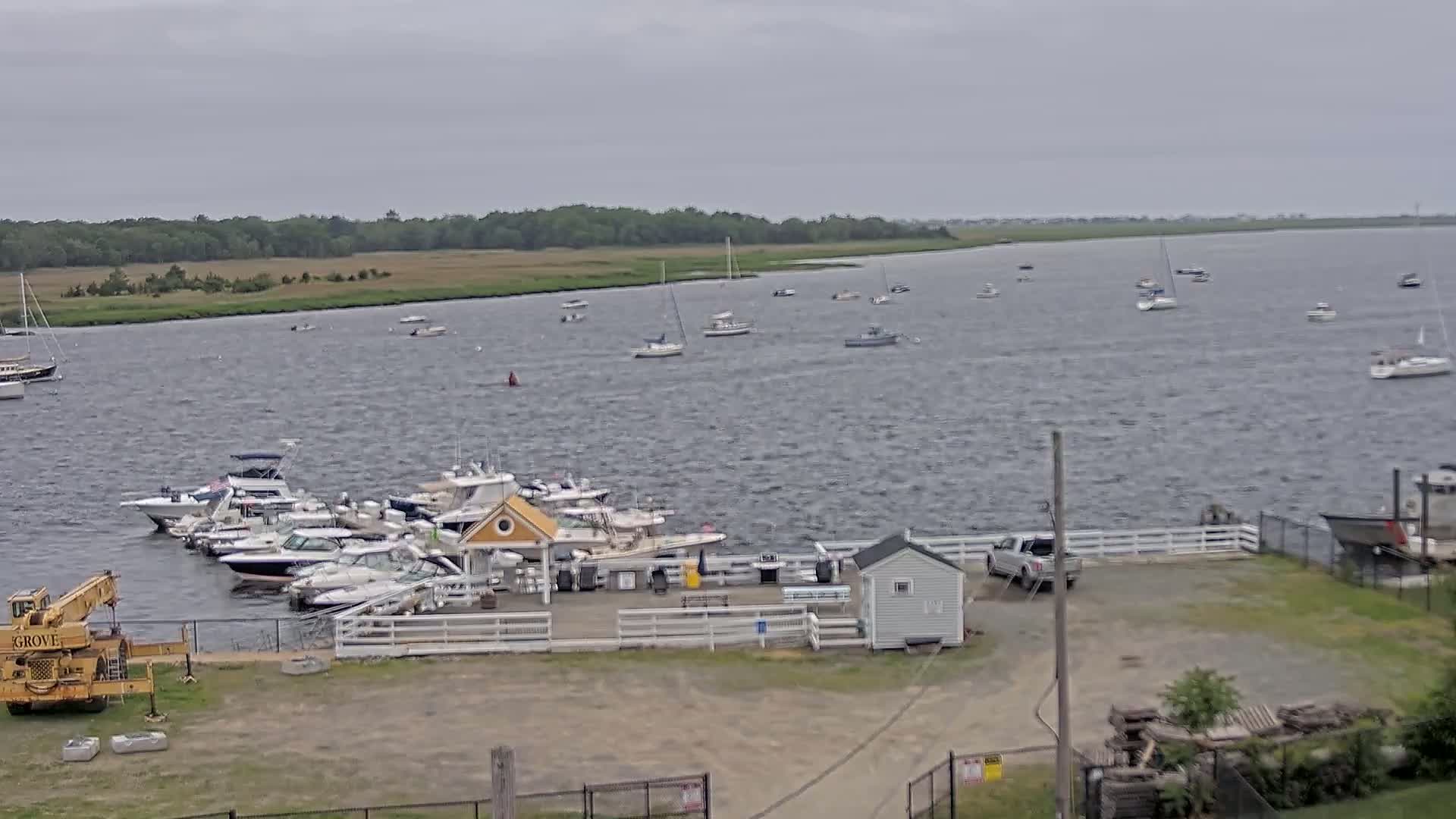 Numerous boats are moored at a marina on a choppy, gray day, with additional boats visible on the water beyond.