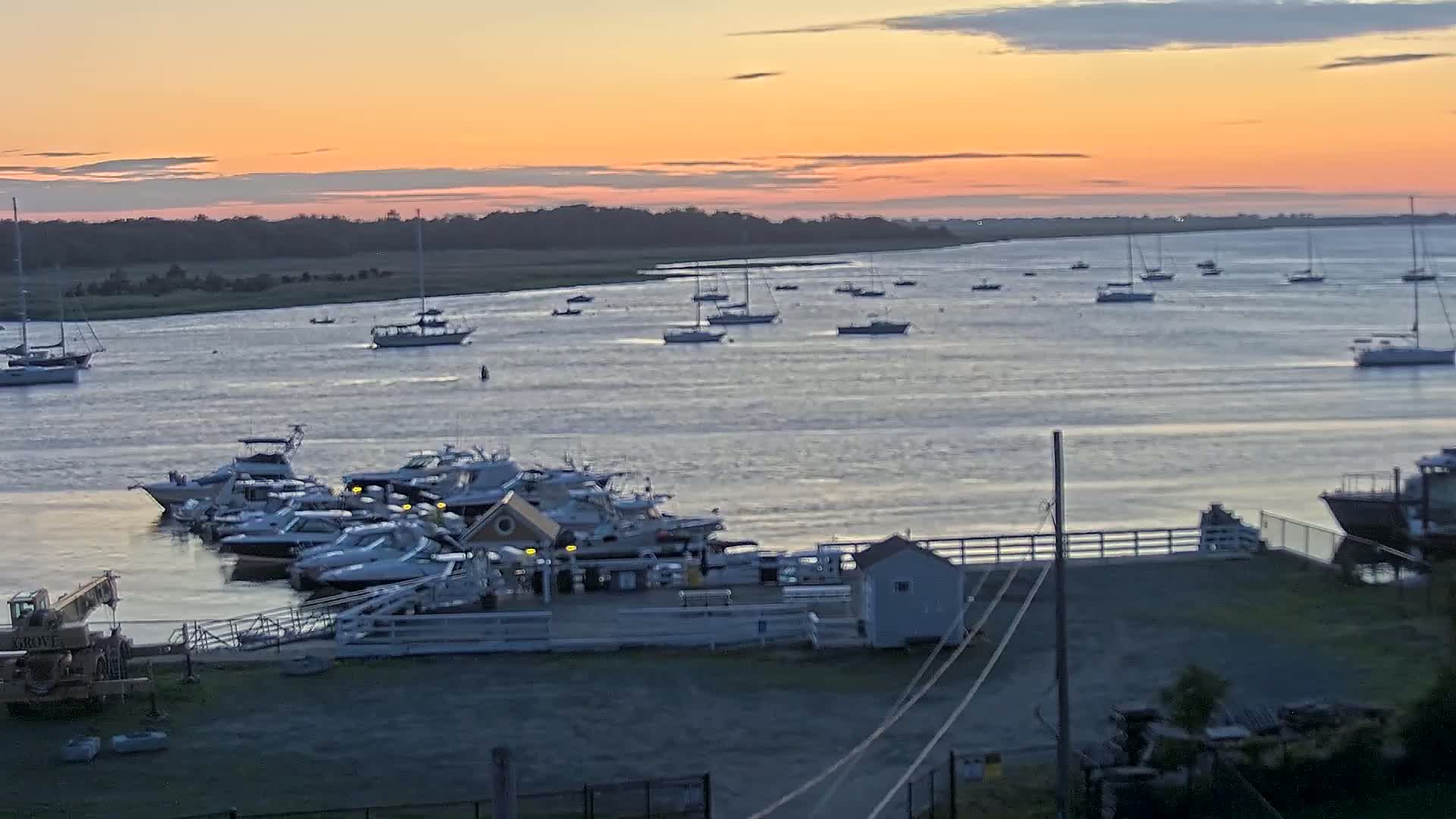 Numerous boats are docked at a marina during a calm sunset over a body of water.