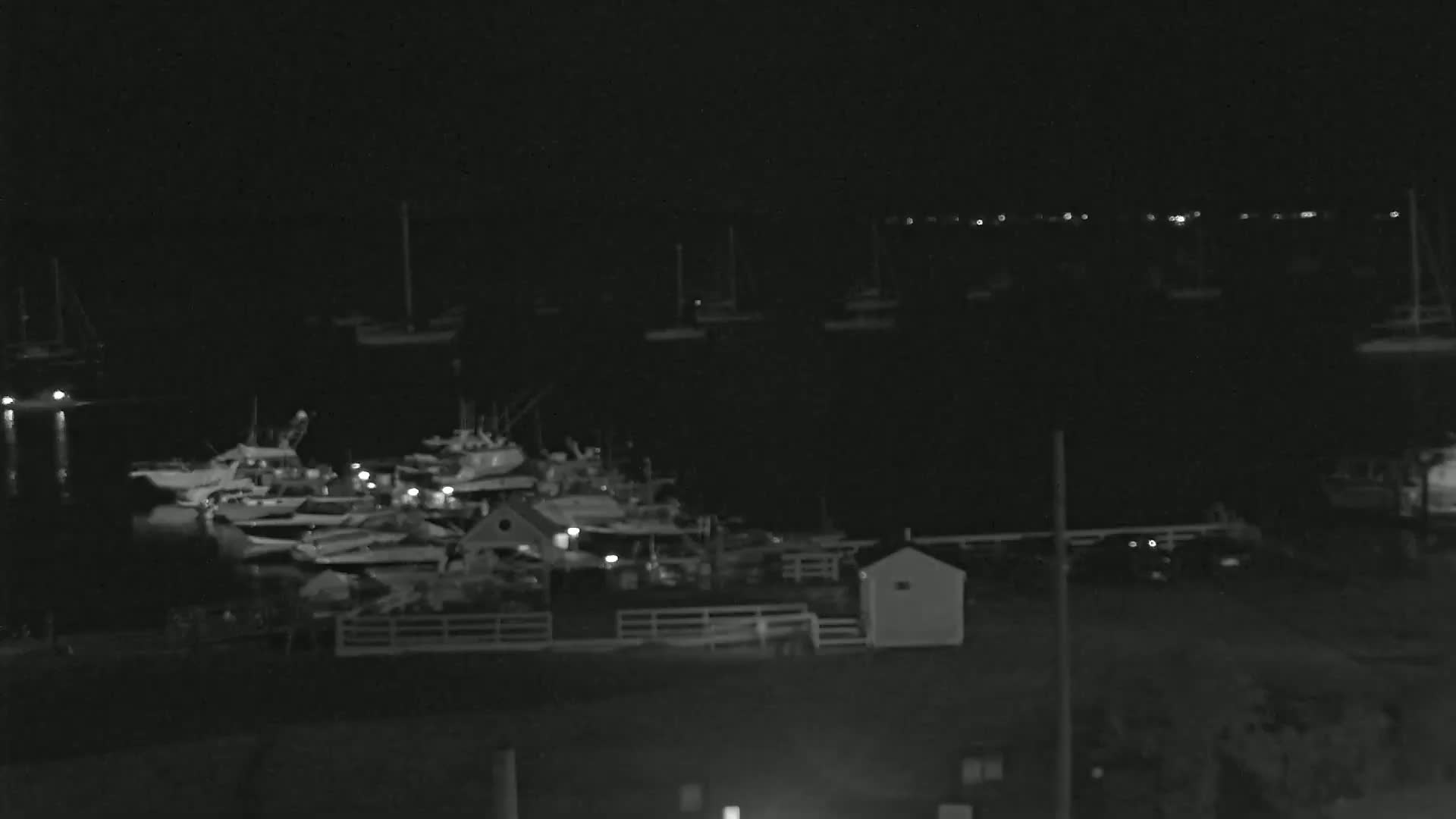 A nighttime view of a harbor filled with numerous boats and small structures, under a dark sky.