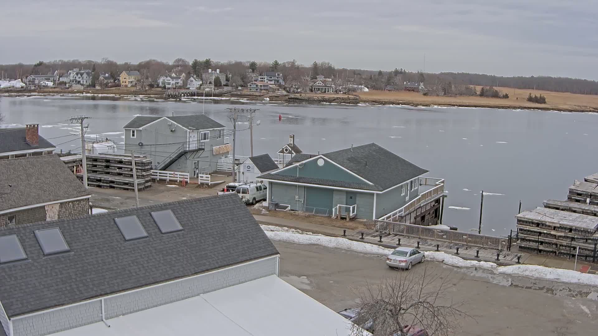 A waterfront town with partially frozen water, houses, and docks under an overcast sky.