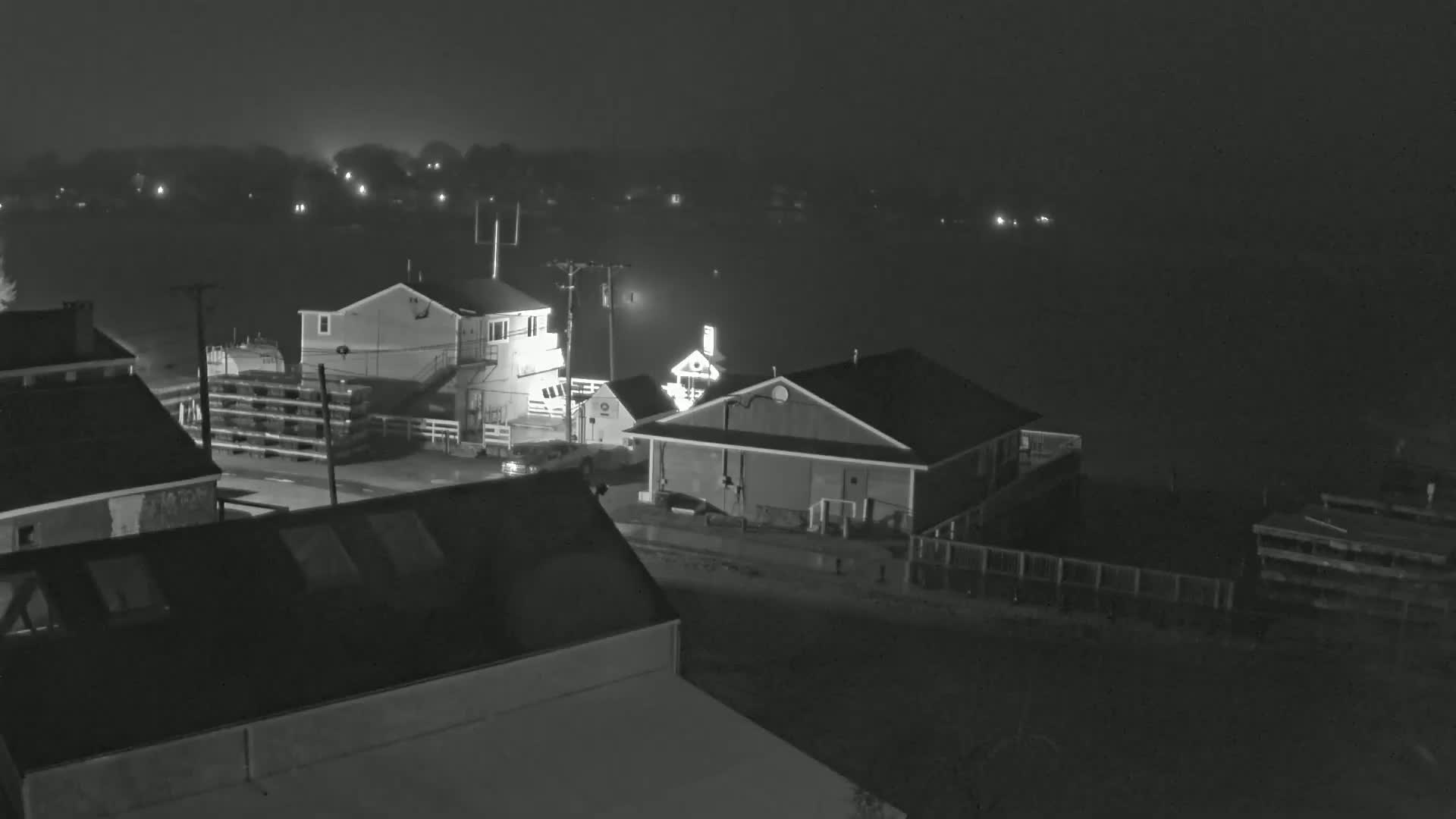 A nighttime, foggy view of several buildings near a body of water, with faint lights visible in the background.