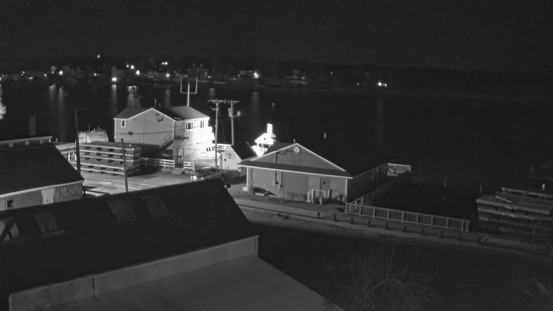 A nighttime, high-angle view of a waterfront area with several buildings, a calm body of water, and some vehicles.