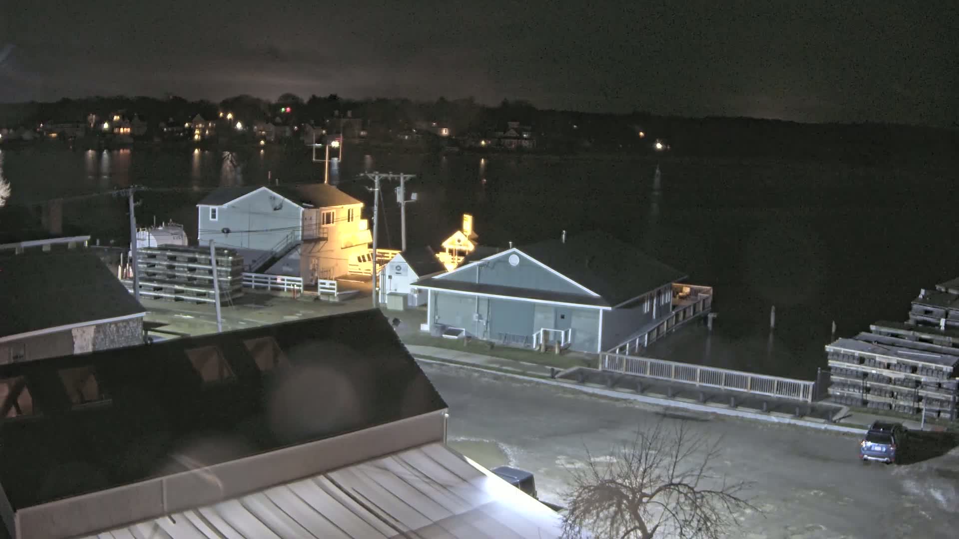 A nighttime, waterfront view shows several buildings near a calm body of water under a dark sky.