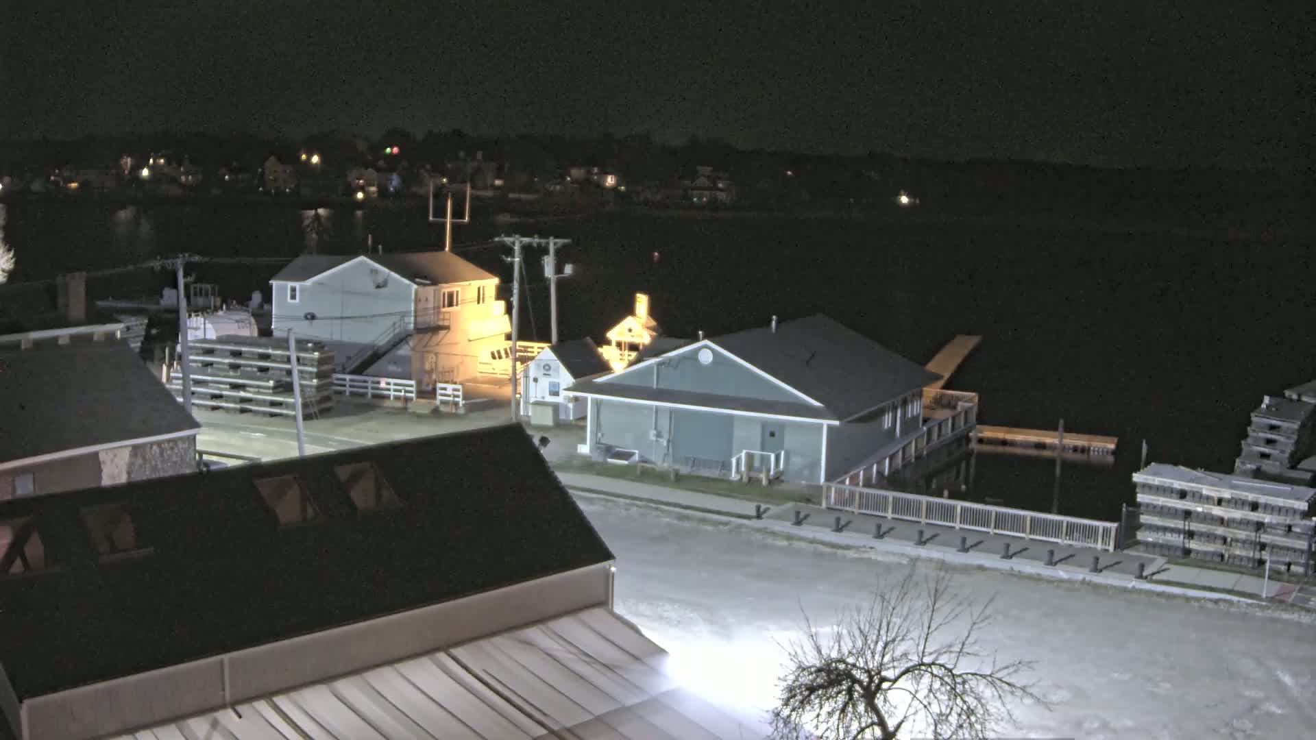 A nighttime aerial view of a waterfront area with several buildings, docks, and lobster traps, under a dark sky.