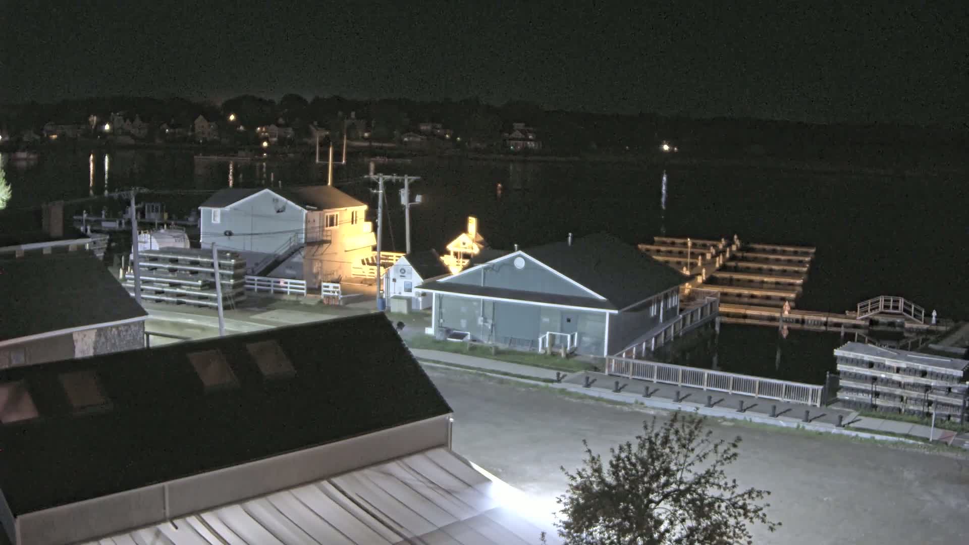 A nighttime view of a waterfront community with several buildings illuminated, a calm body of water, and boat docks.