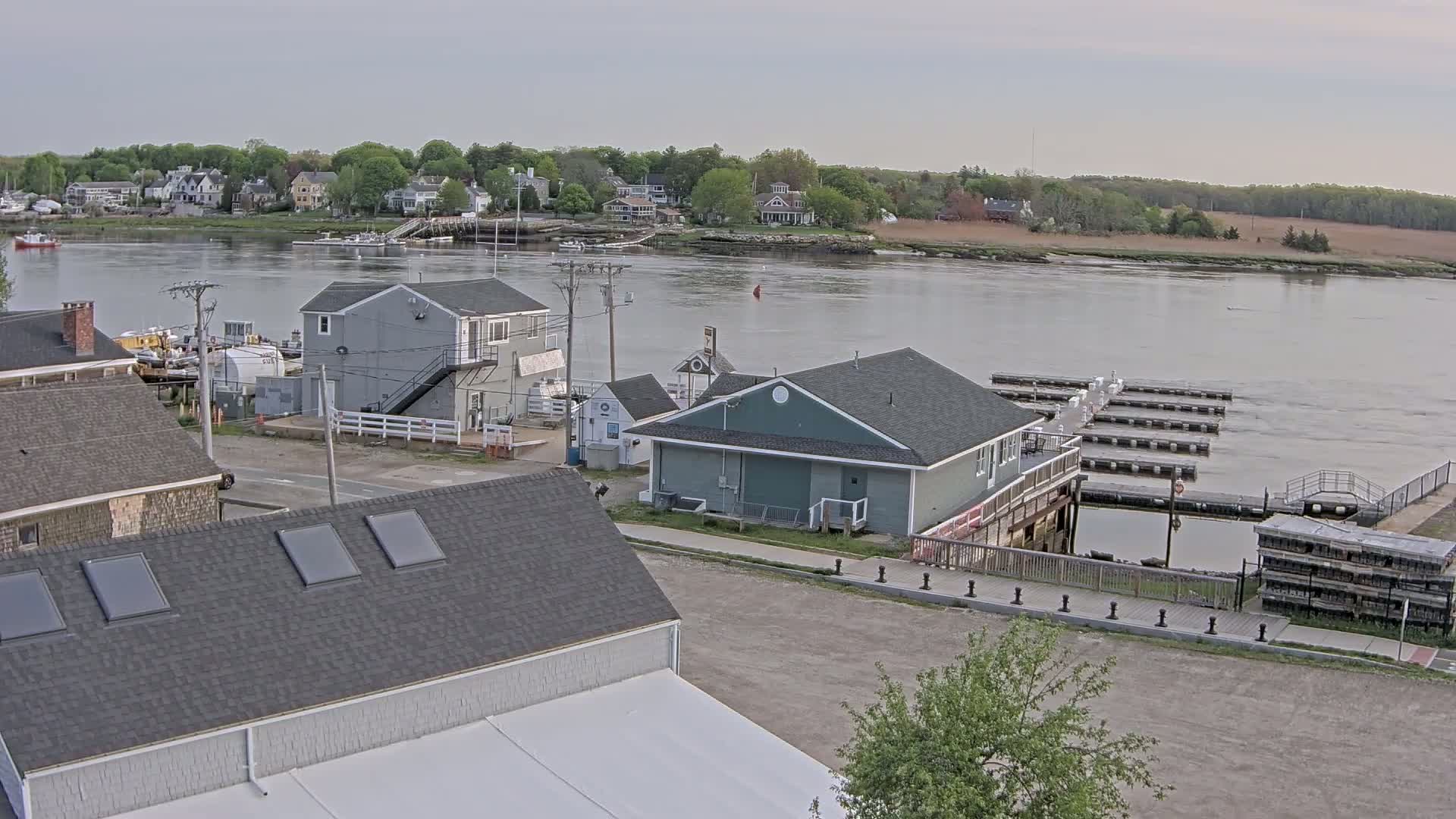 An overcast day reveals a waterfront scene with several buildings, a marina with numerous docks, and a river flowing past a line of houses.