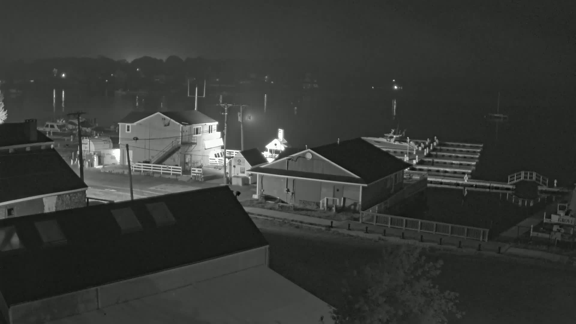 A nighttime, foggy view of a waterfront area with several buildings, docks, and boats.