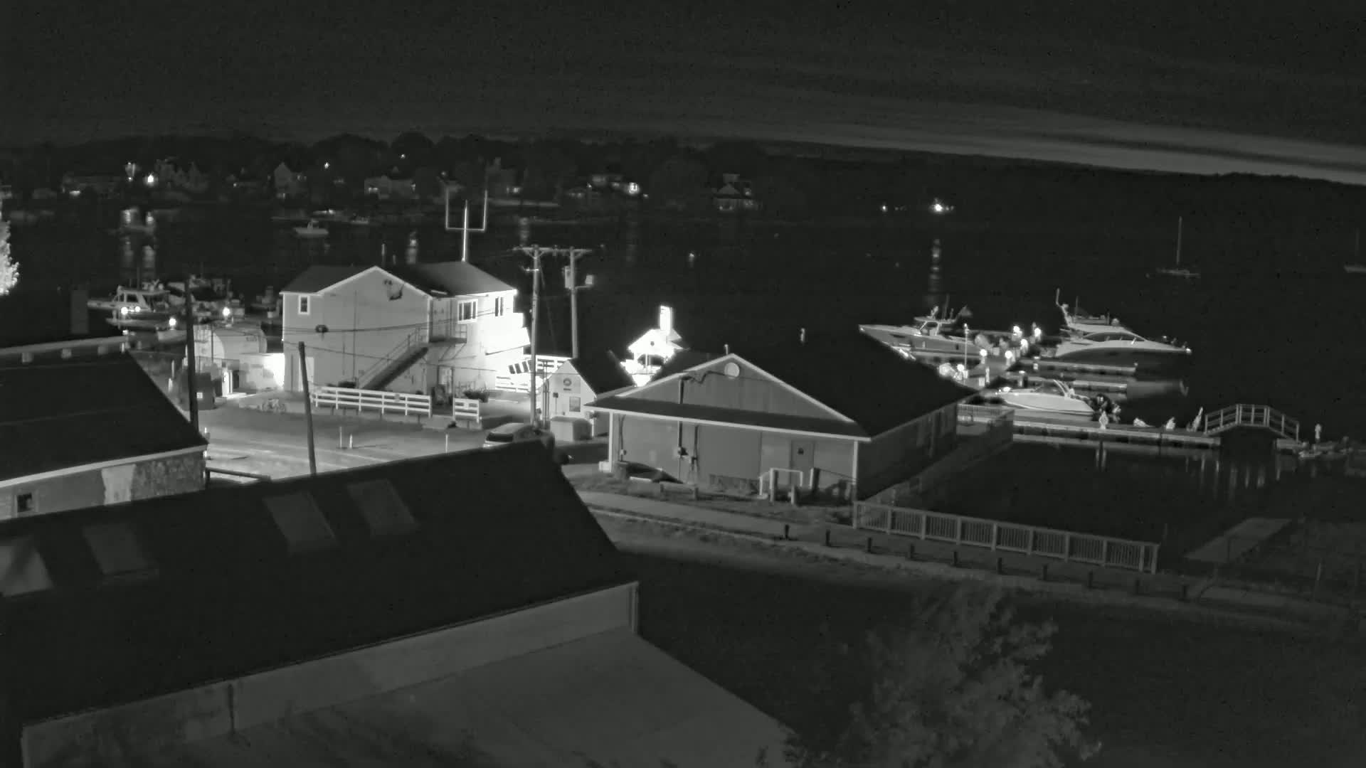 A nighttime view of a harbor with several boats docked, alongside buildings and a roadway.