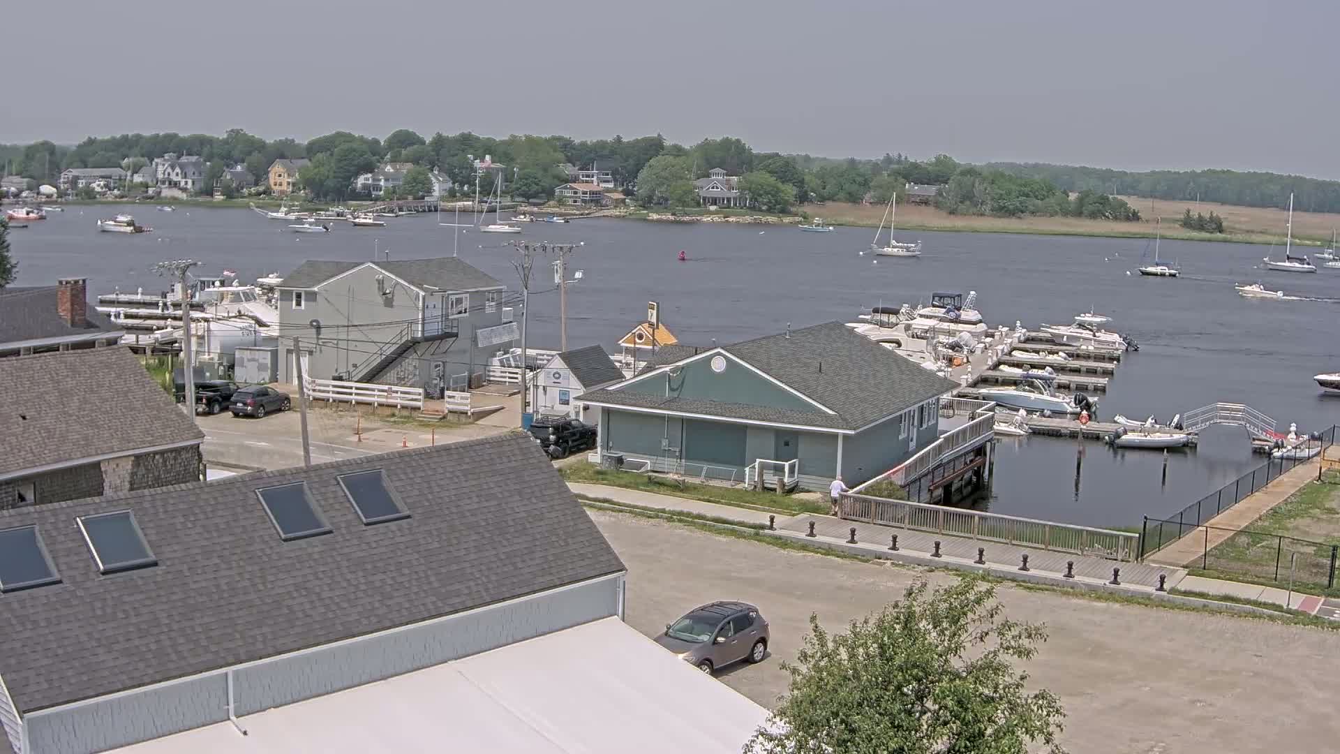 A marina with numerous boats docked, surrounded by houses and a calm body of water under a clear sky.