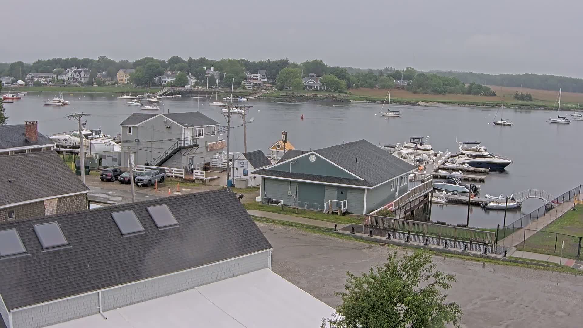 A marina with numerous boats, adjacent buildings, and a calm body of water under an overcast sky.