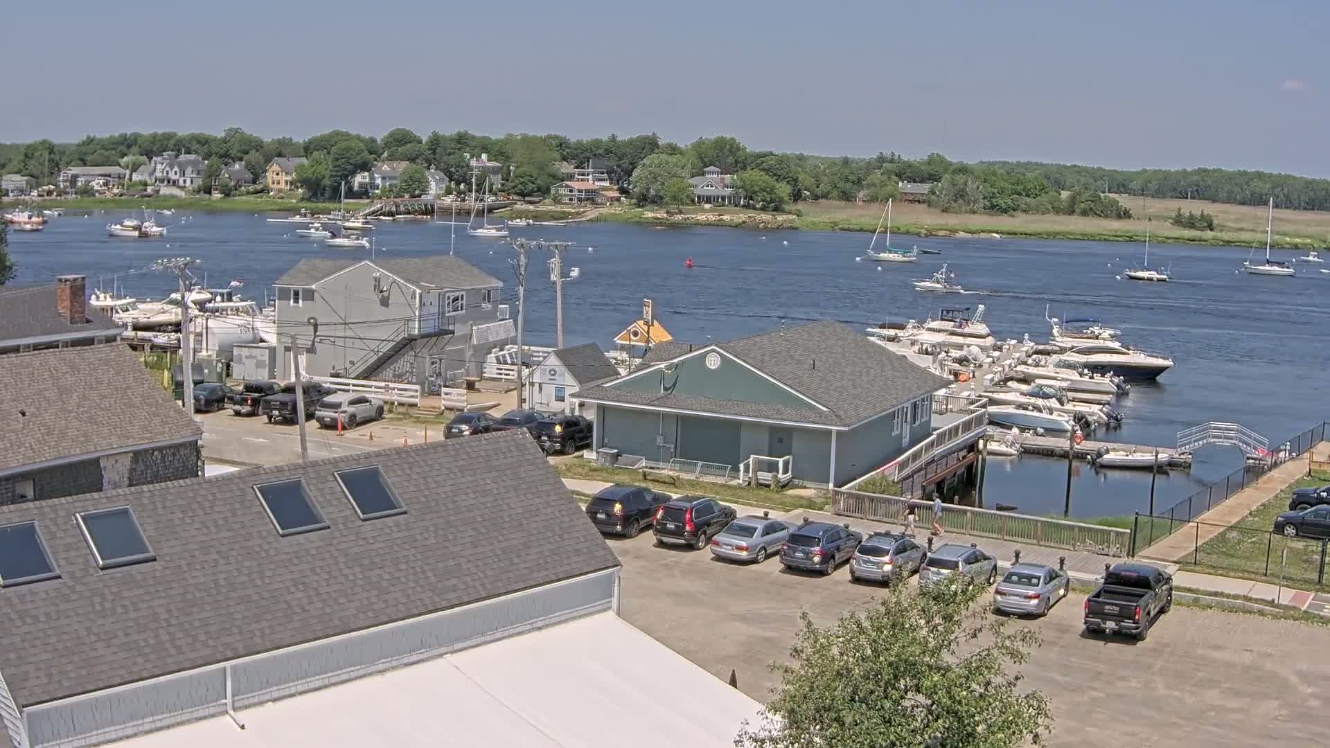 A marina with numerous boats docked, surrounded by buildings and cars, on a sunny day.