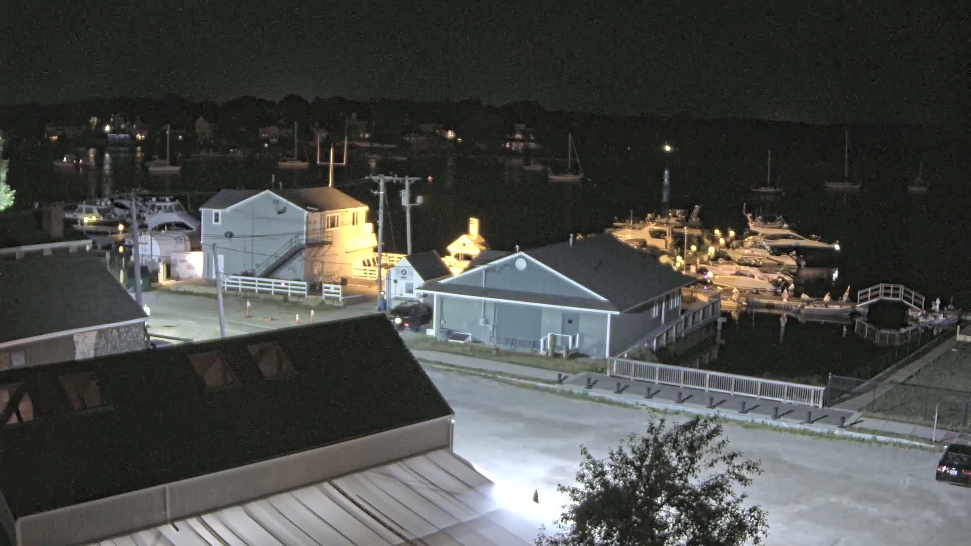 A nighttime aerial view of a marina with docked boats and surrounding buildings under a clear, dark sky.