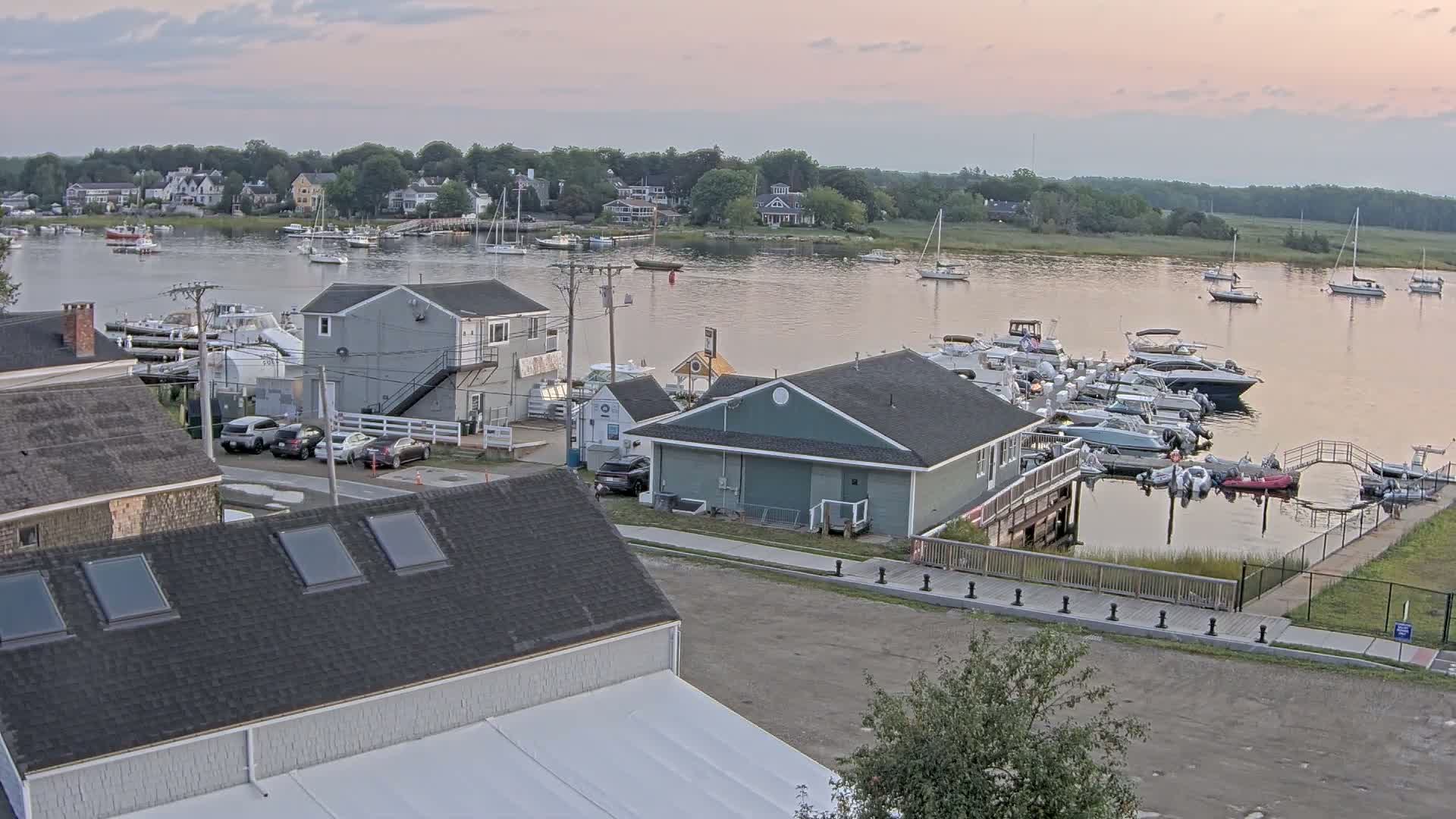A nighttime, black-and-white view of a waterfront area with several buildings, cars, and numerous boats docked at a marina under a clear sky.