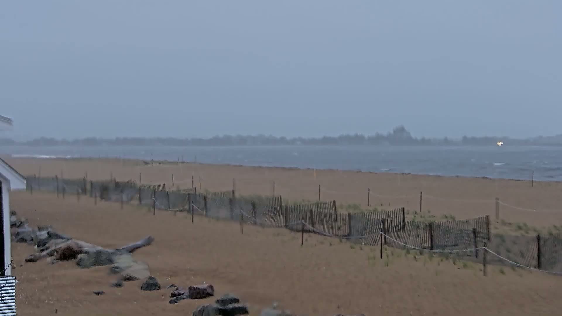 A sandy beach with a low wooden fence stretches to a choppy grey sea under an overcast sky.