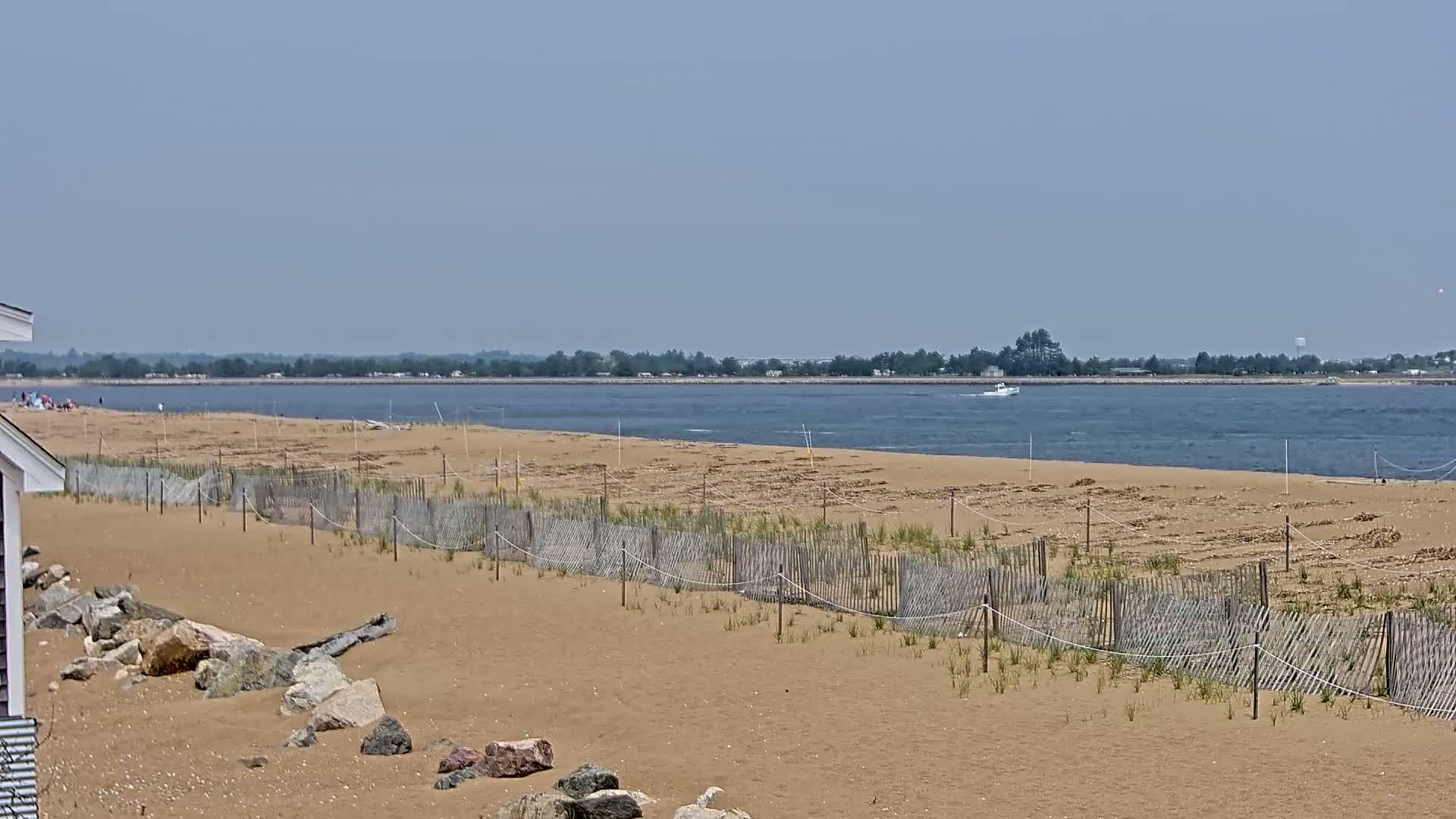 A sandy beach with low wooden fences and a small boat on calm water under a clear sky.