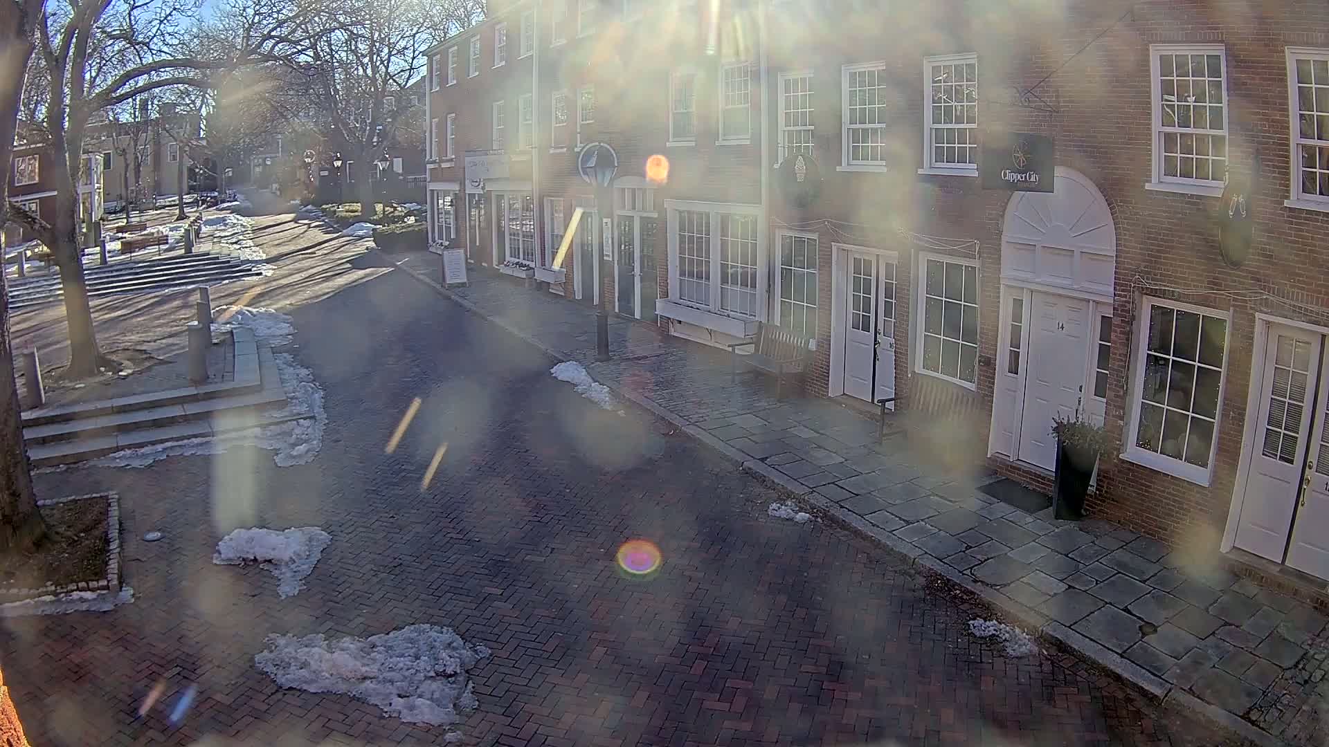 A sunny winter day on a brick street lined with brick buildings, patches of snow on the ground and sidewalks.