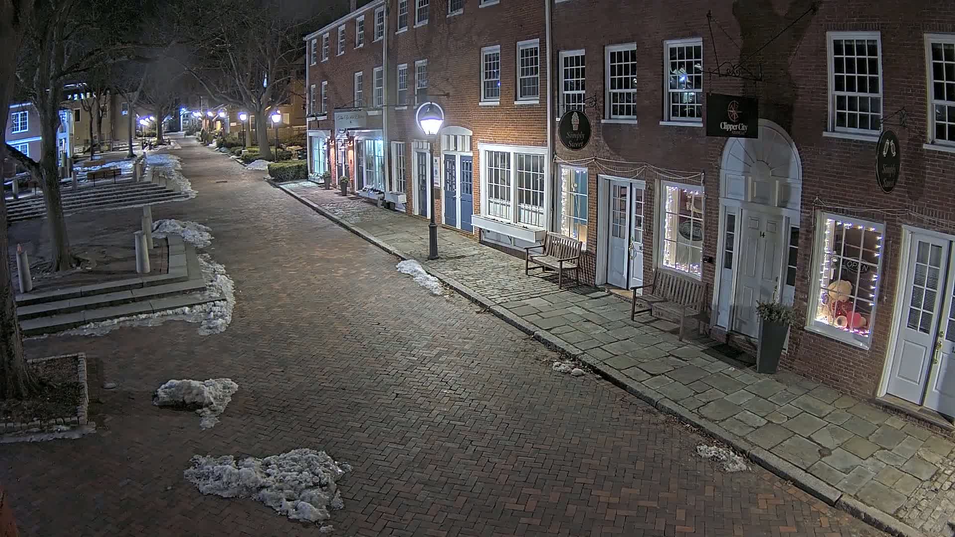 A brick street lined with illuminated brick buildings at night, with patches of snow on the ground.