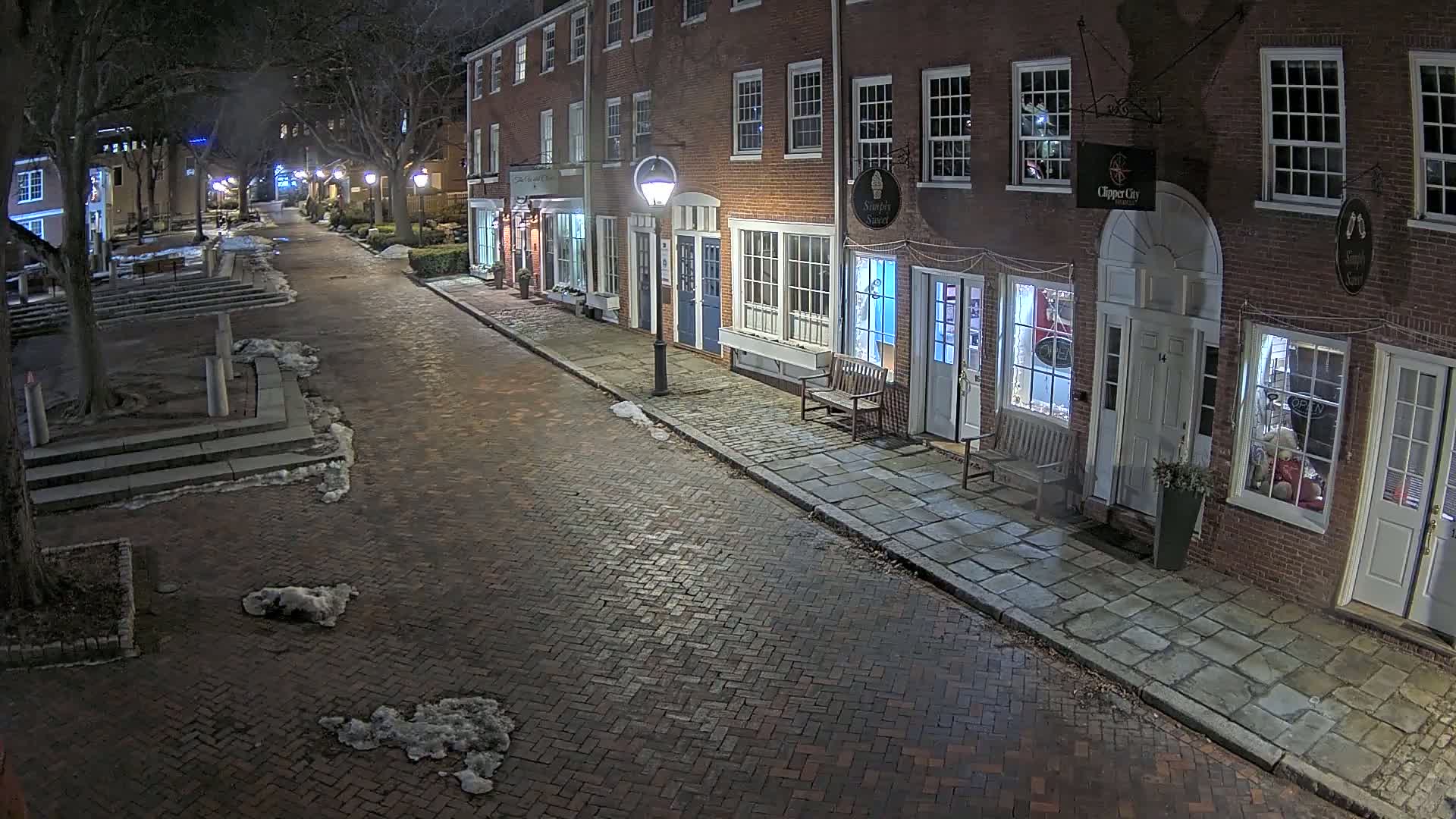 A brick street at night, lined with brick buildings and a few patches of snow on the ground.