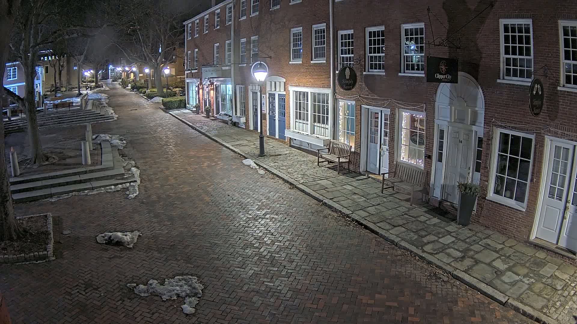 A brick street lined with brick buildings at night, with patches of snow on the ground.