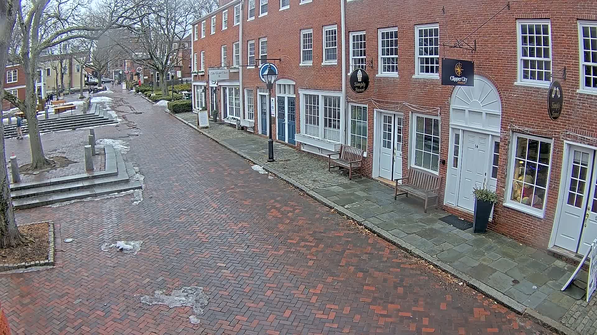 A brick street lined with brick buildings on a partly cloudy day with patches of snow and ice on the ground.