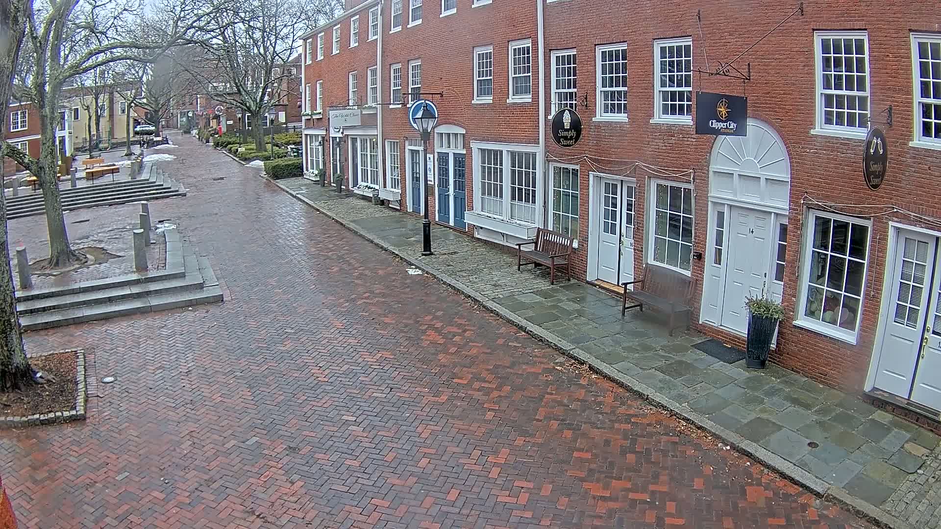 A brick street lined with brick buildings on a cloudy day, with some snow or ice patches visible on the ground.