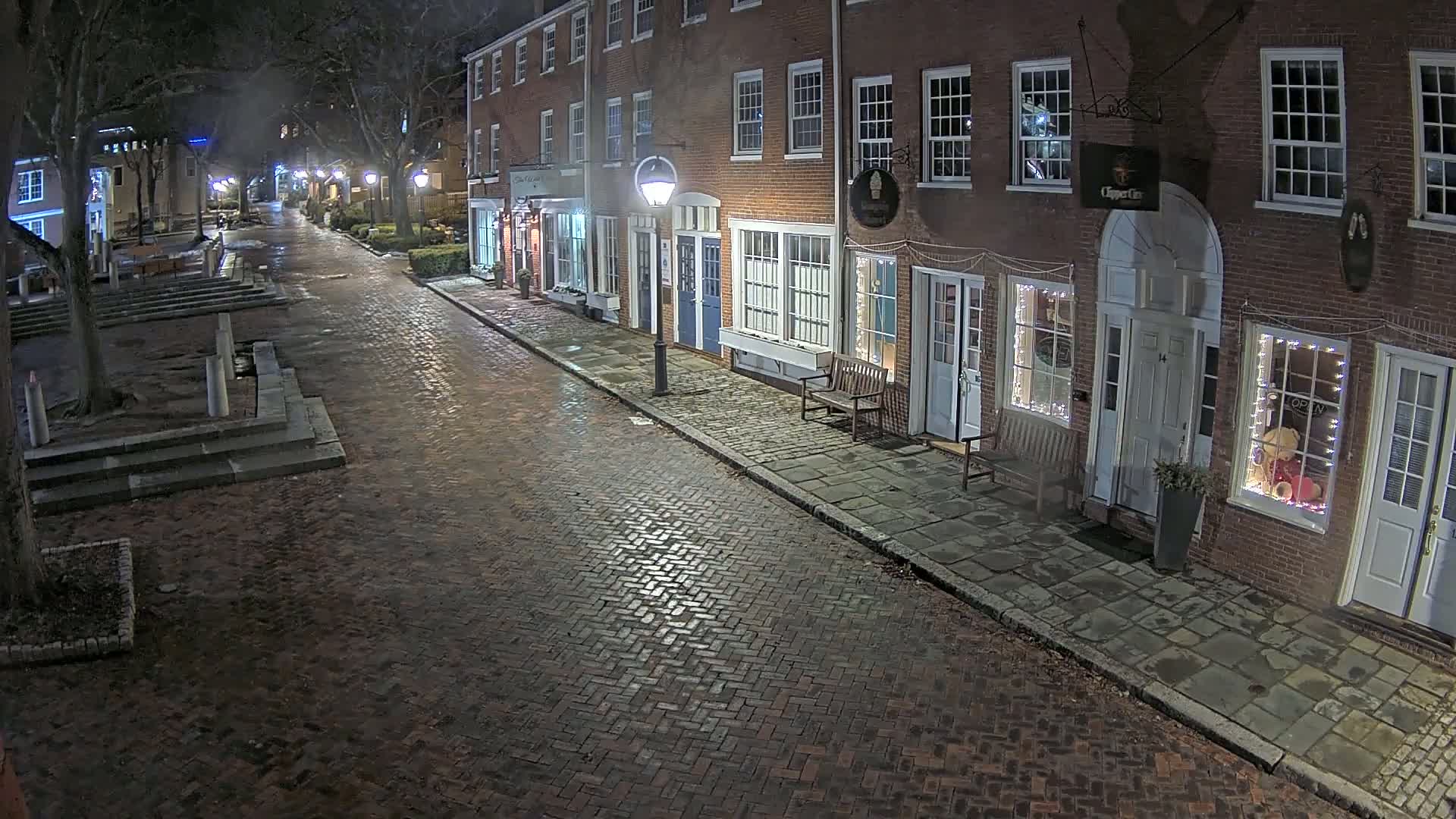 A wet brick street at night lined with illuminated brick buildings.