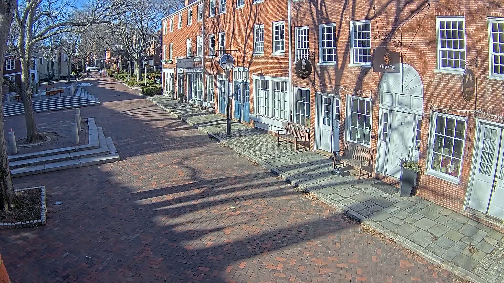 A brick-paved street lined with brick buildings casts long shadows on a sunny day.