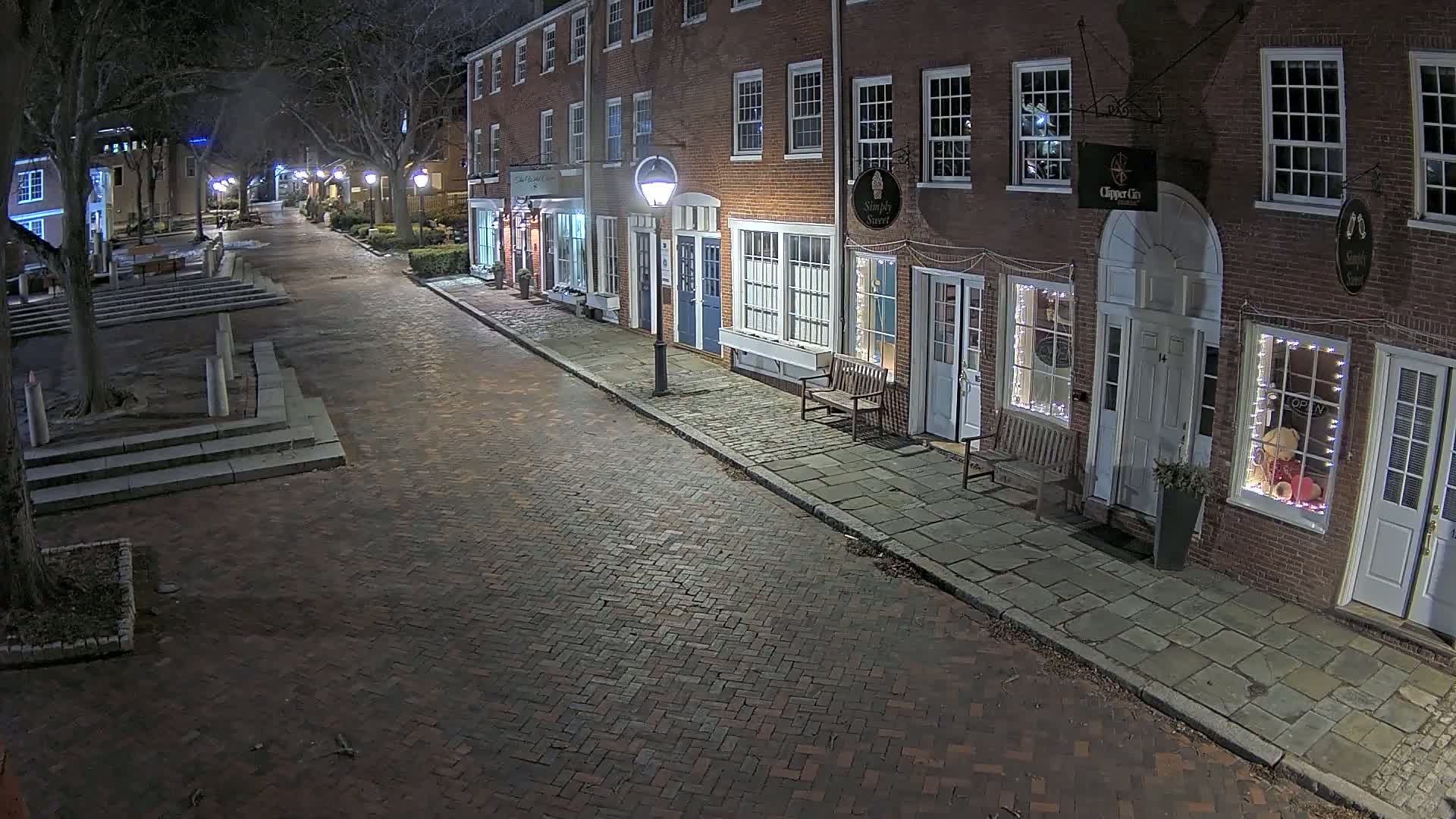 A brick street lined with brick buildings at night, illuminated by streetlights.