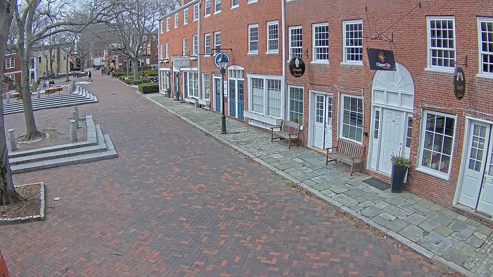 A brick-paved street lined with brick buildings on a cloudy day.