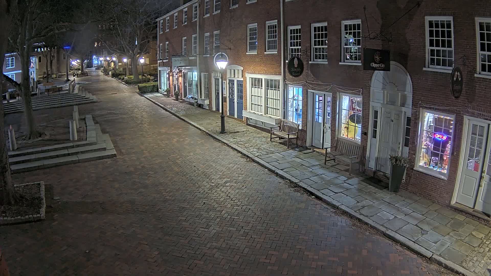A brick street lined with illuminated storefronts in brick buildings at night.