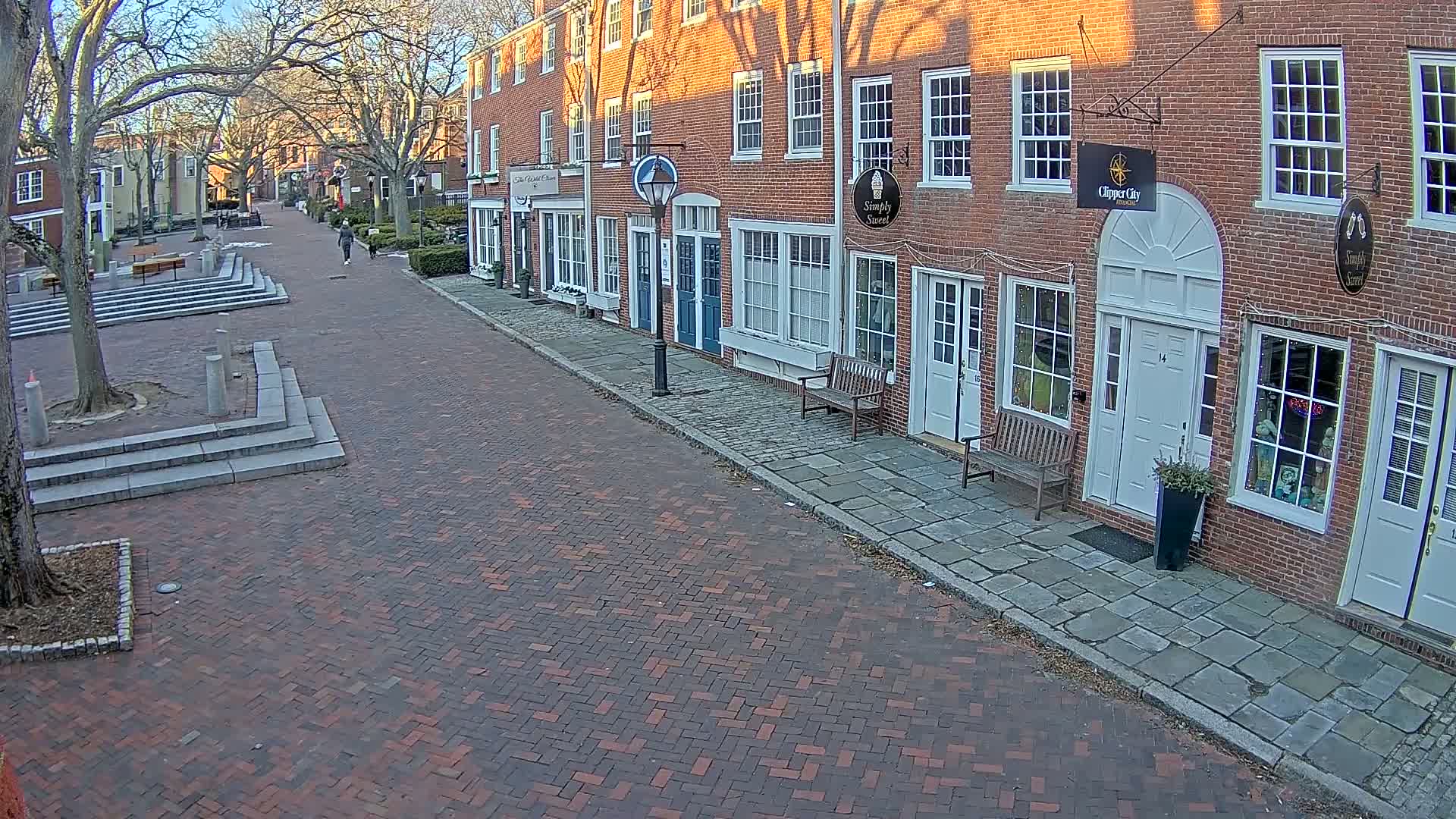 A brick-paved street lined with brick buildings on a sunny day, with a person walking in the distance.