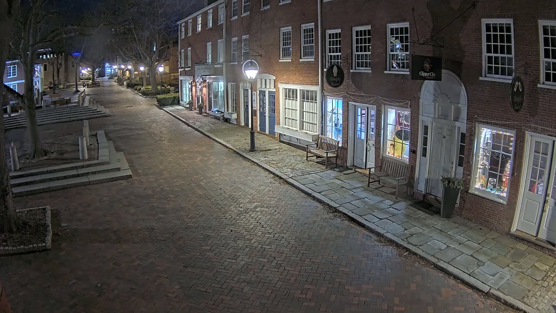 A brick street lined with brick buildings at night, illuminated by streetlights.