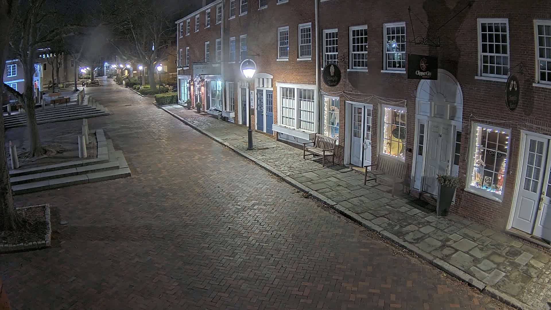 A brick street at night, lined with brick buildings and lit by streetlights, shows a mostly empty scene under a hazy sky.